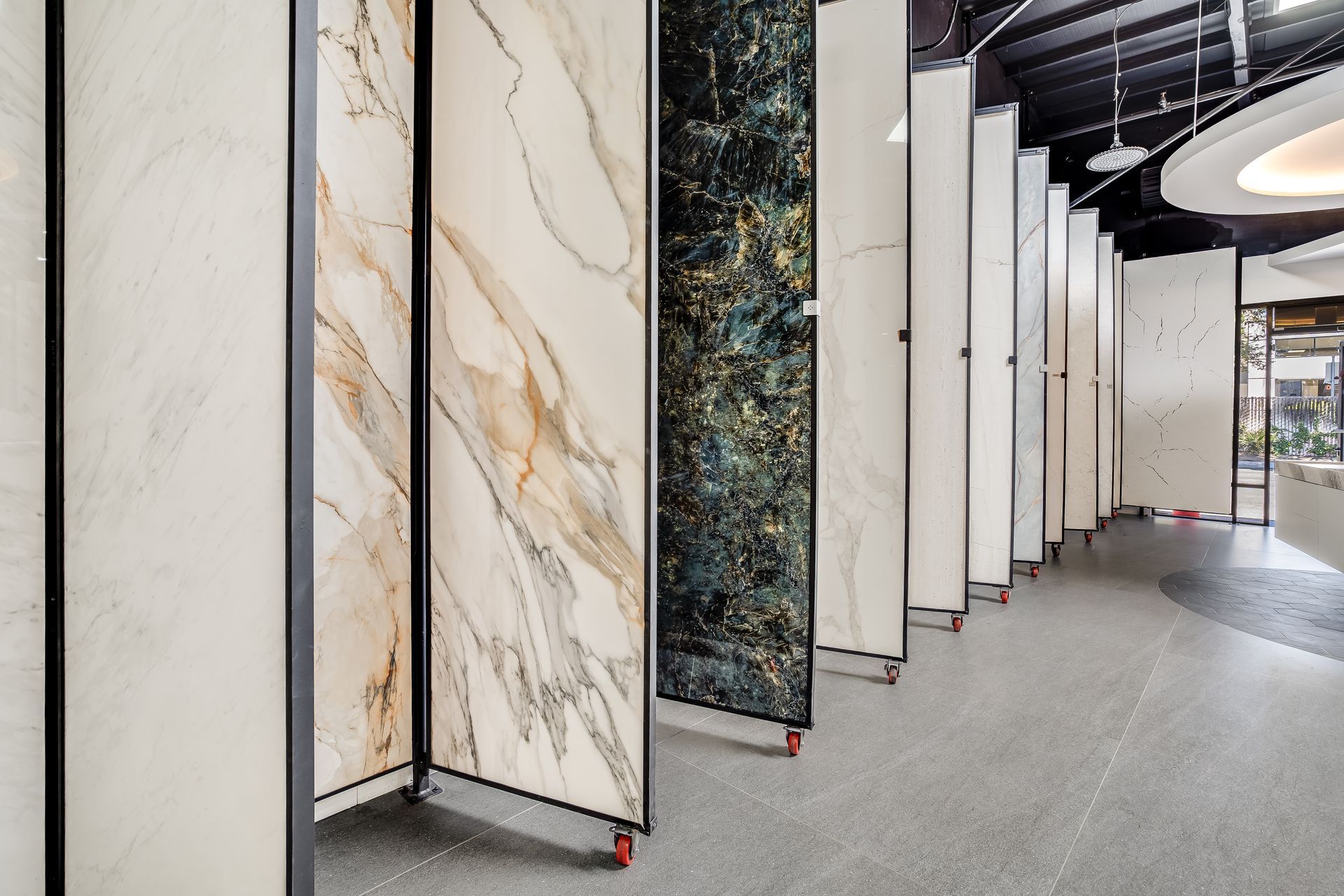 Row of large marble slabs in a showroom, with white, beige, and dark veined stone panels on display.
