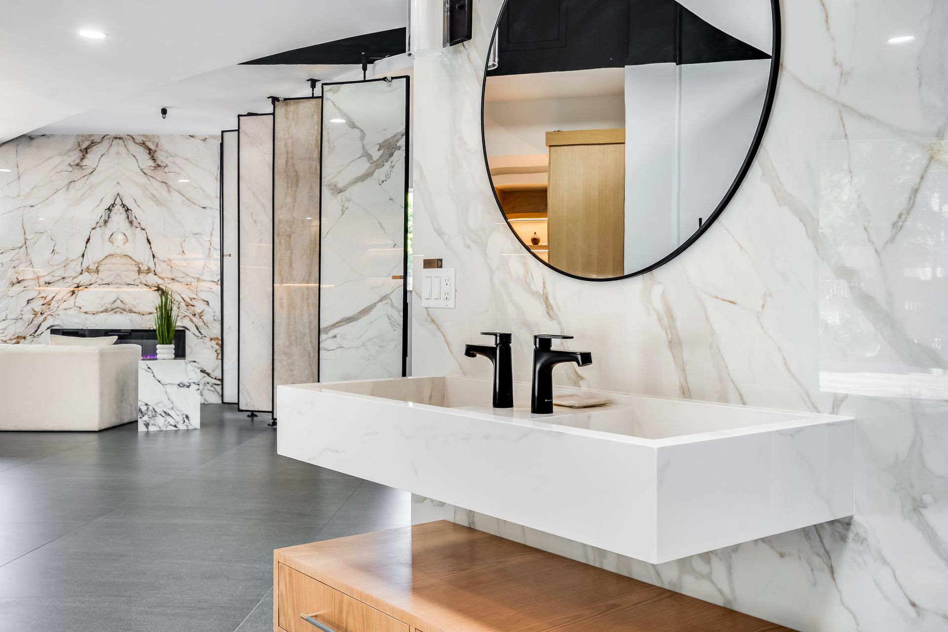Modern bathroom with white marble walls, black fixtures, and a round mirror over a floating sink.