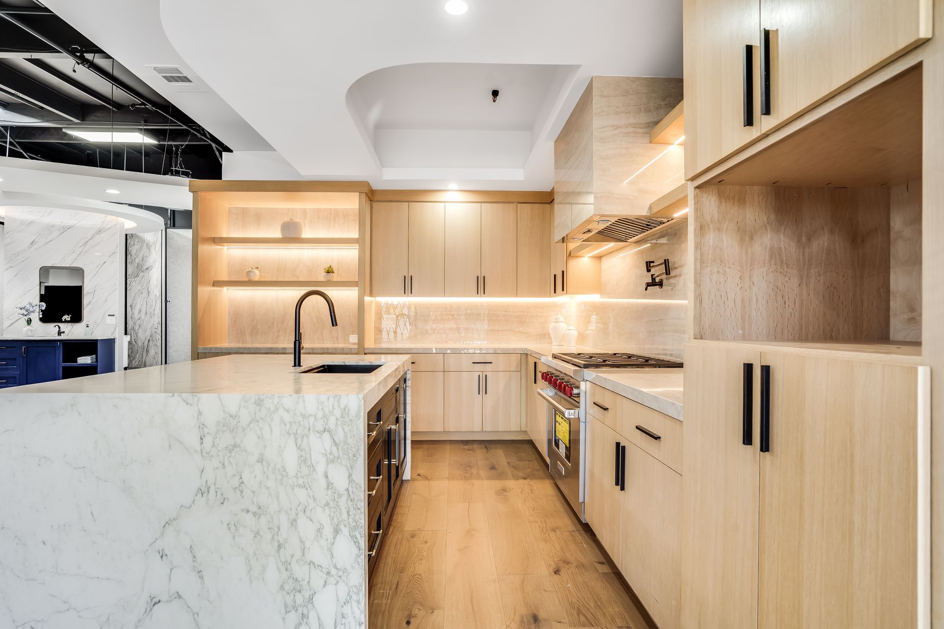 Modern light-wood kitchen with marble island, black fixtures, and built-in shelving