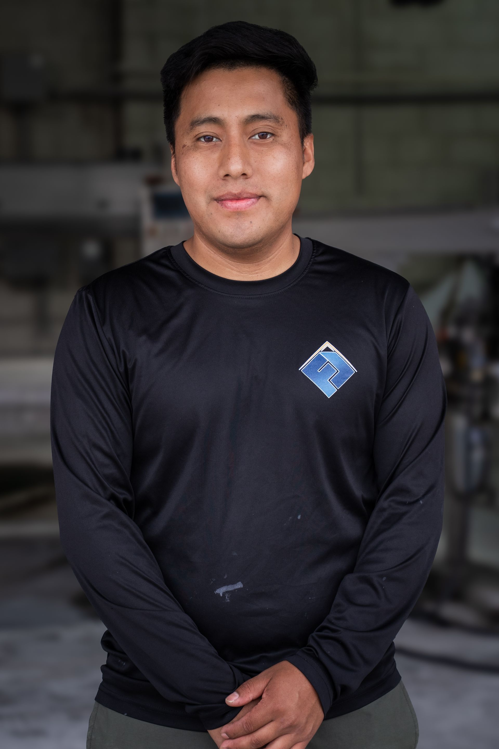 Person standing indoors wearing a black long-sleeve shirt with a small blue logo.