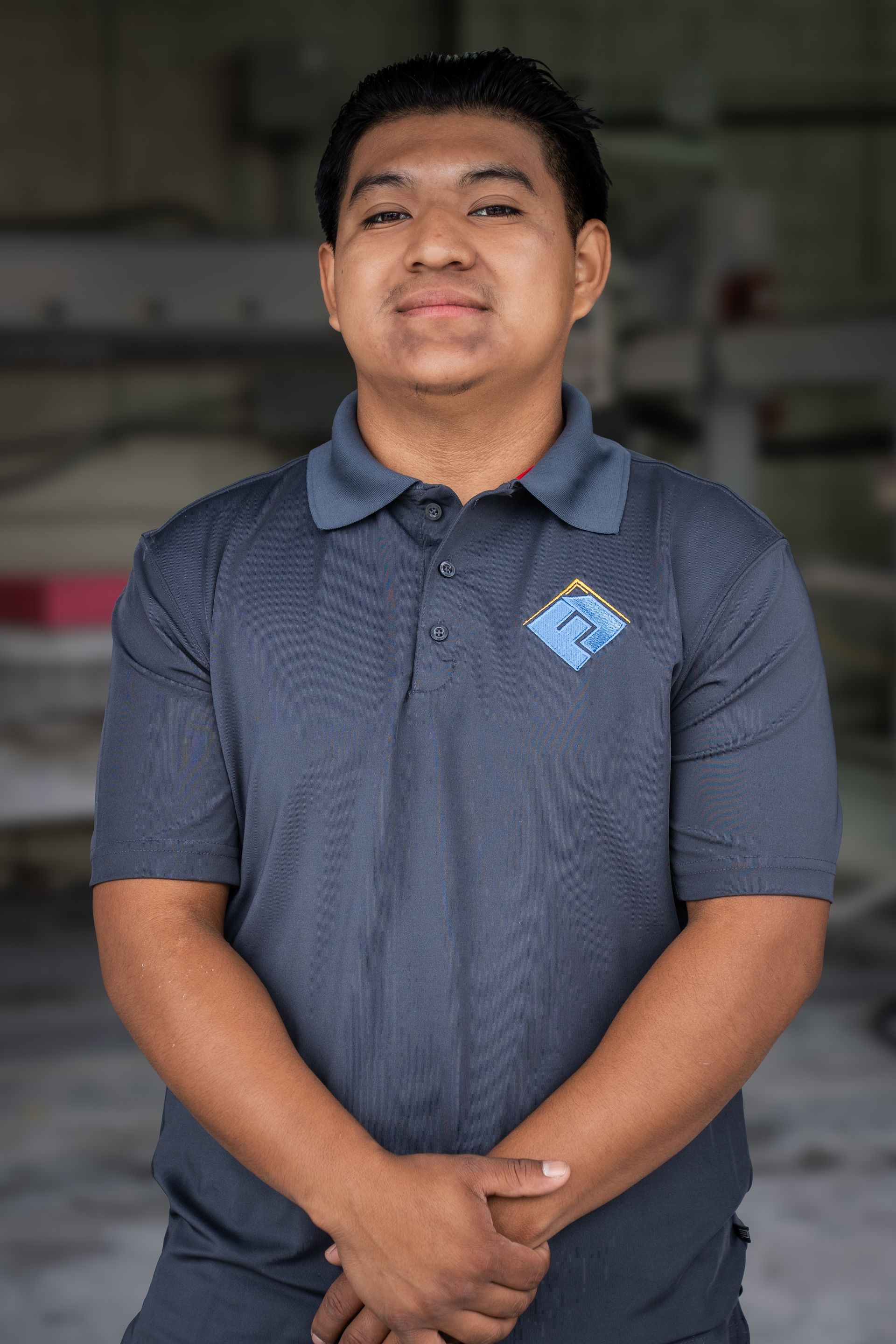 Person in a blue polo shirt standing indoors with hands clasped, facing the camera.