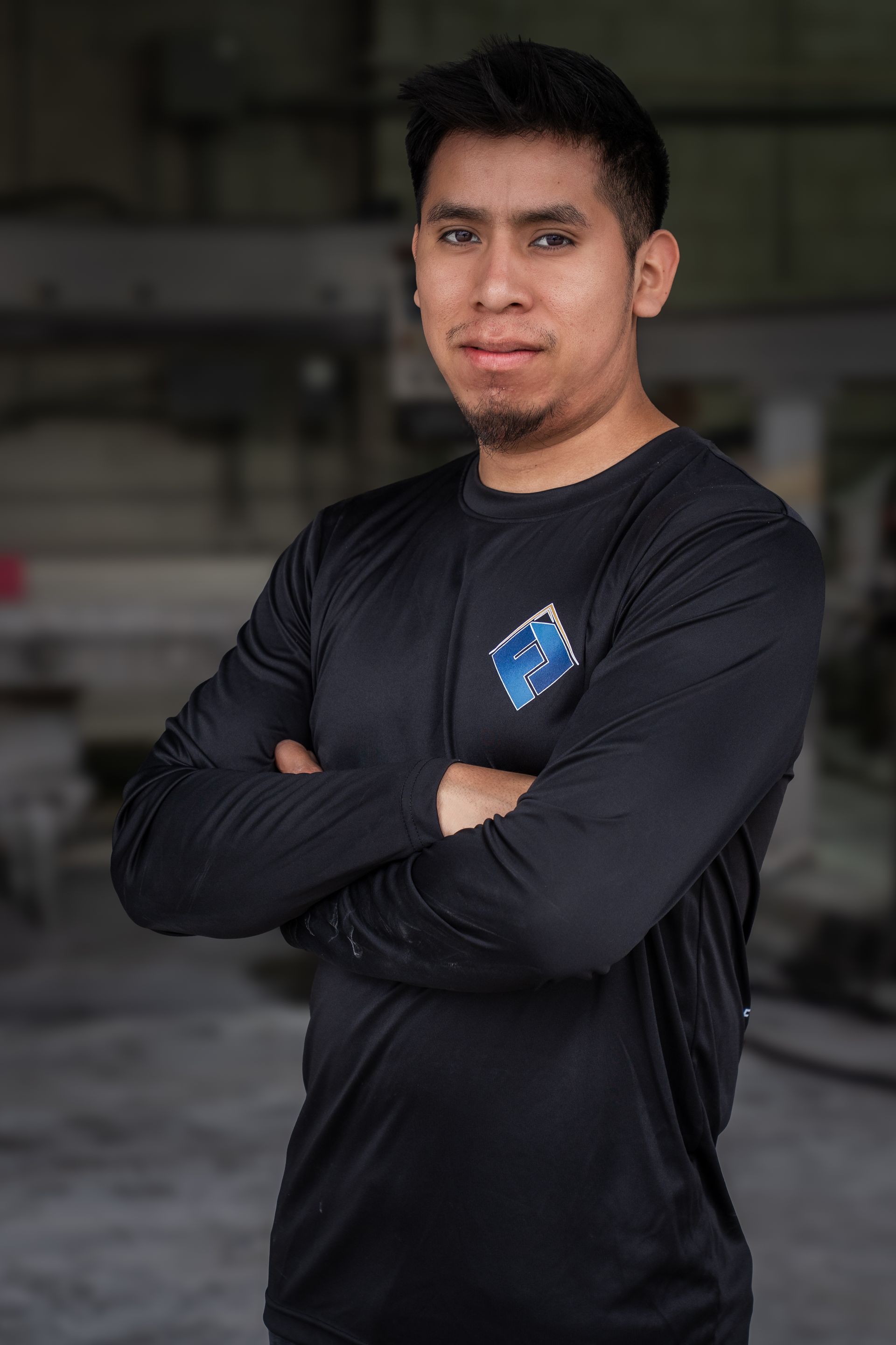 Person in a black long-sleeve shirt standing with arms crossed against a blurred indoor background