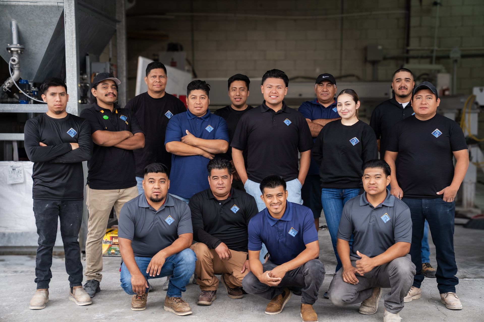 Group of workers in navy shirts posing outside a building entrance, some standing and some crouching.