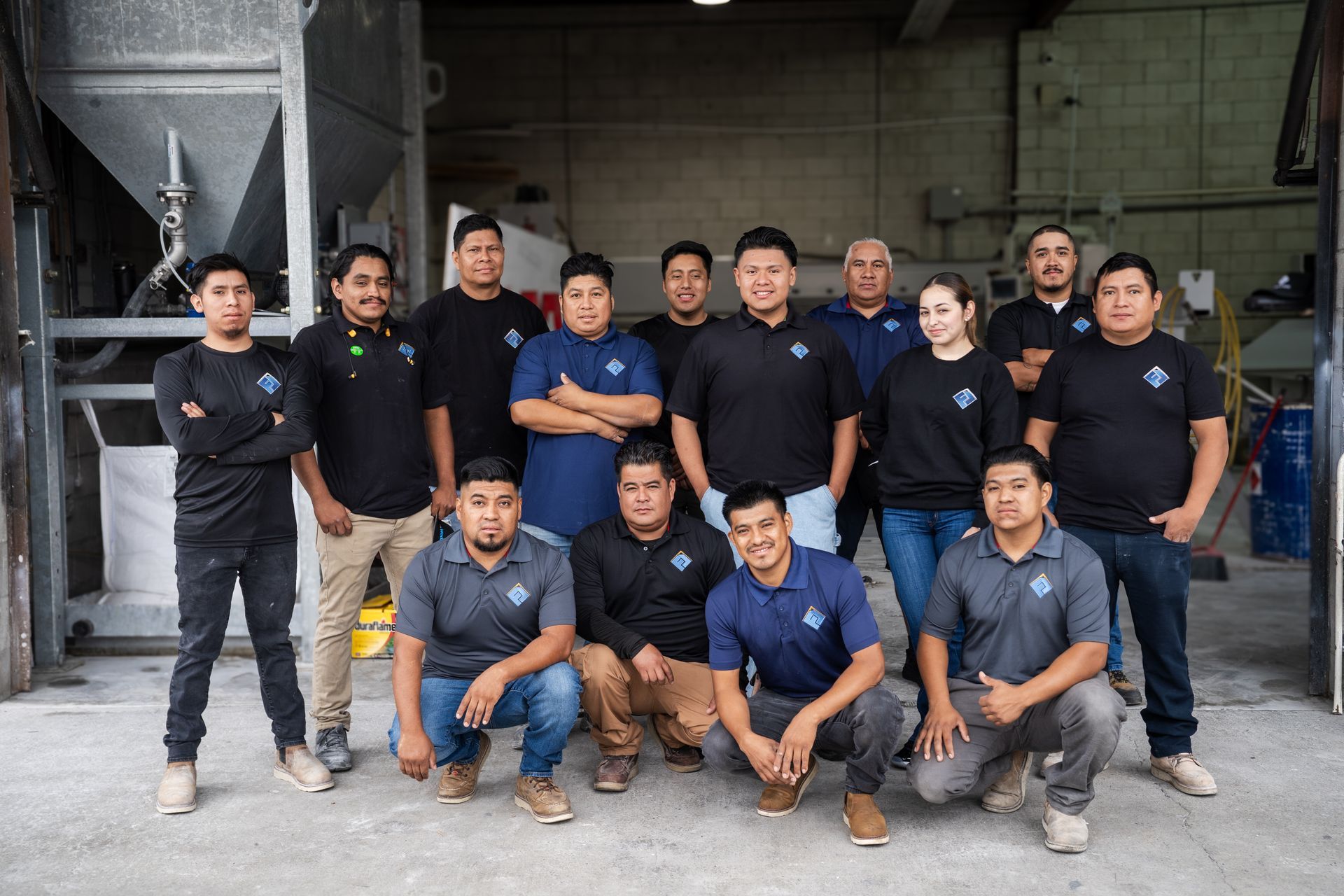 Group of 12 people in navy shirts posing together in a warehouse-like industrial space