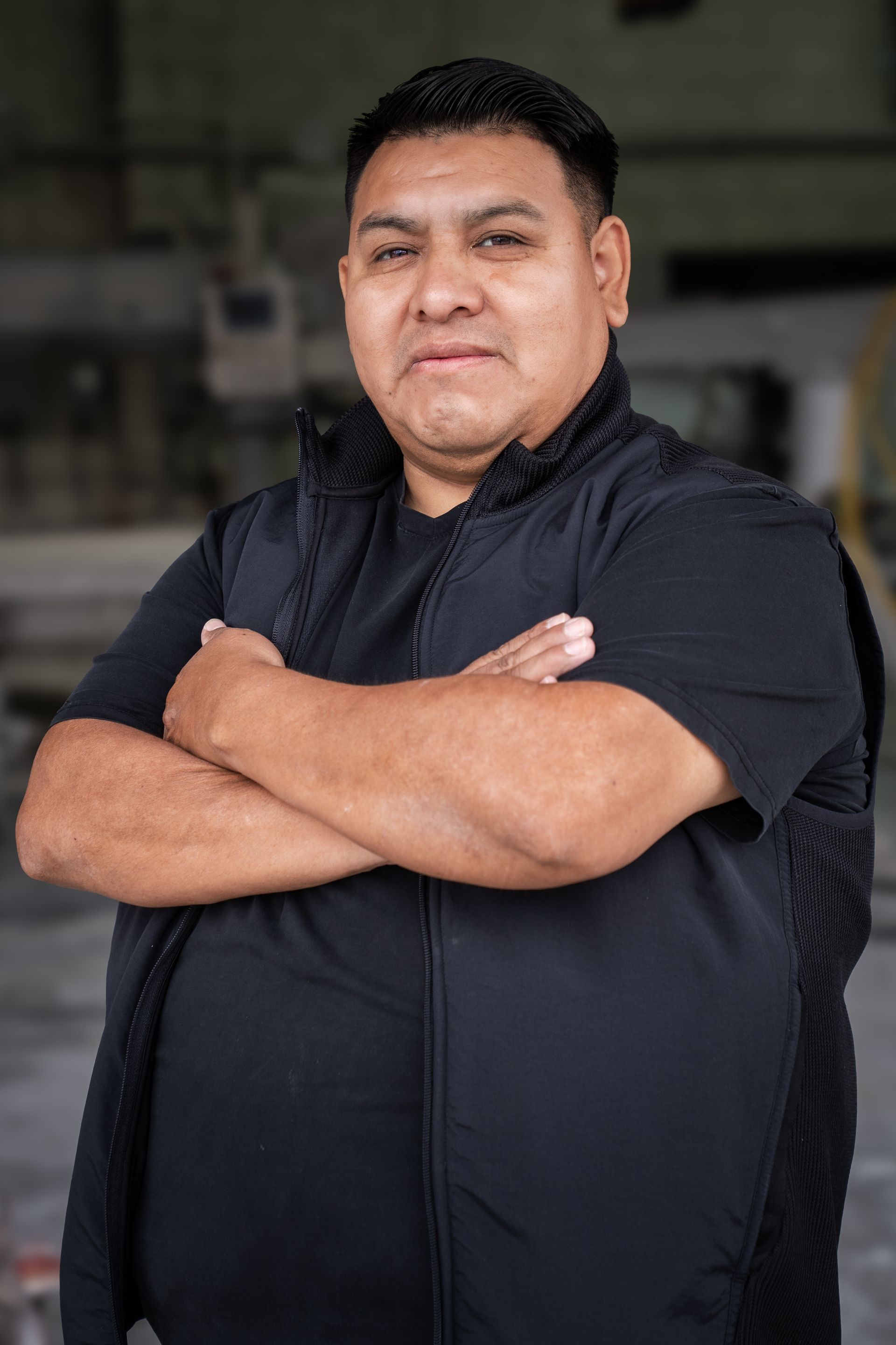 Person in a black shirt with arms crossed, standing indoors and facing the camera.