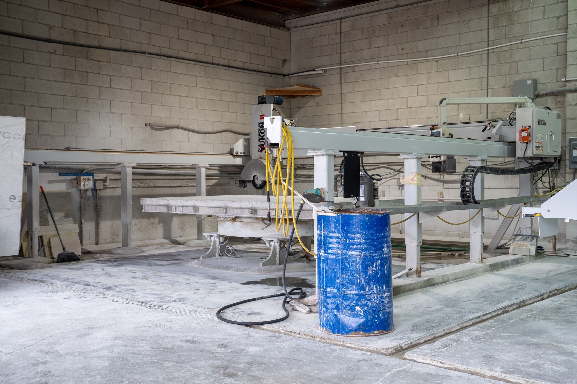 Industrial workshop with a CNC machine, blue barrel, and white dust-covered floor and walls