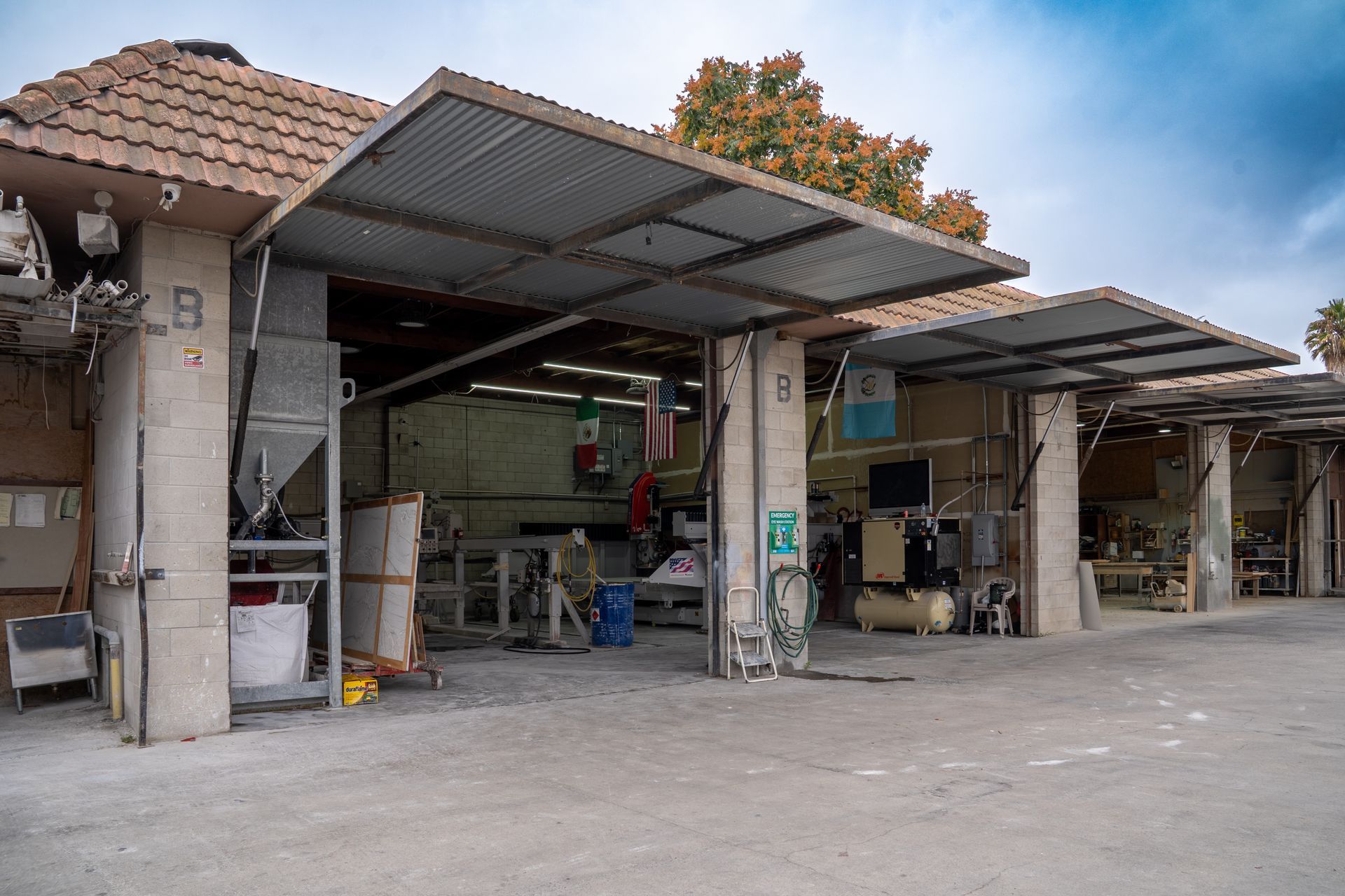 Open-air workshop with metal roof, concrete pillars, and tools inside a rustic garage