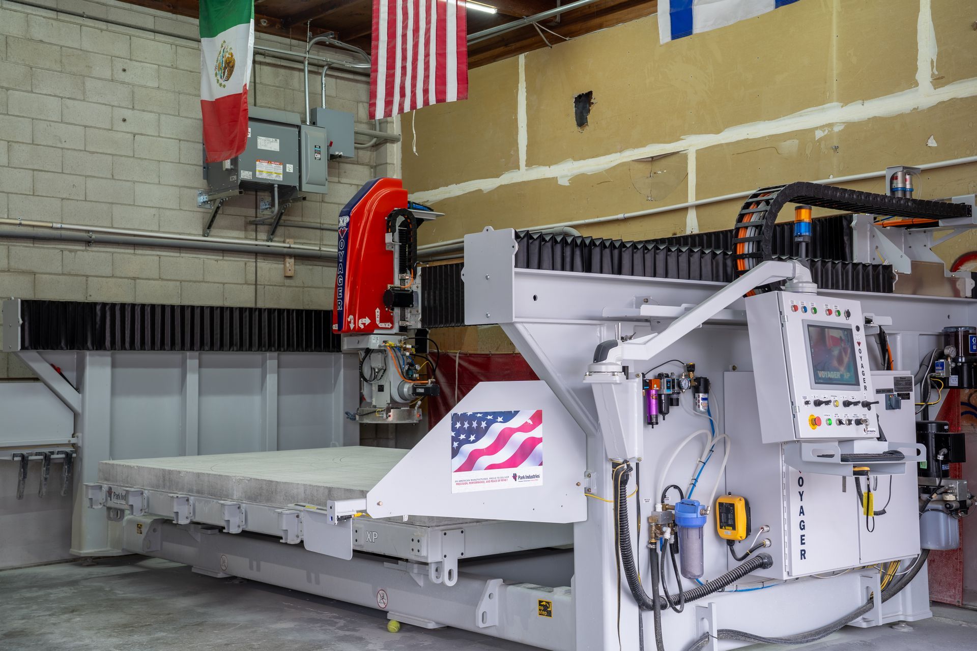 Large white industrial machine in a warehouse, with red piping and control panels under a US flag.