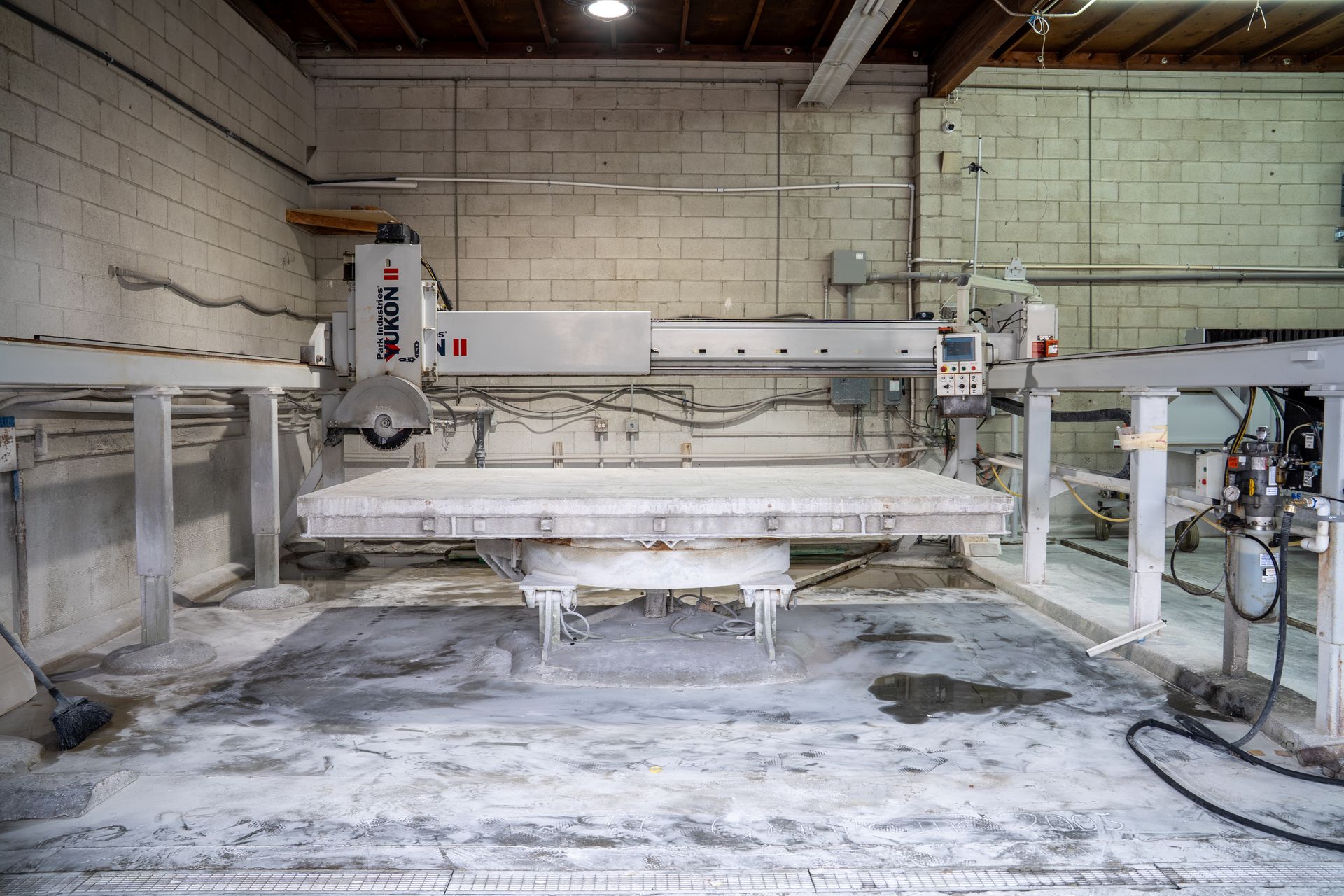 Large industrial machine in a dusty workshop, with a white cutting bed and rails against cinderblock walls.
