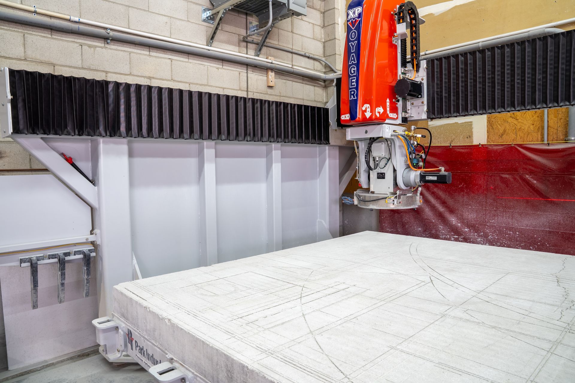 Industrial CNC machine cutting a white foam block in a workshop with gray walls and red equipment.