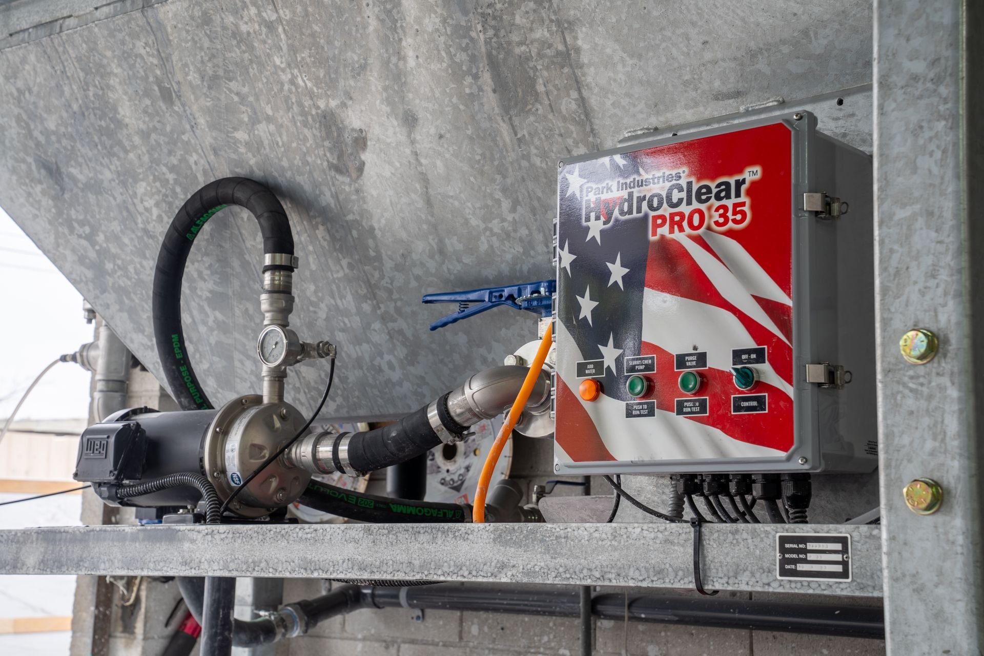 Red industrial control box with hoses and wires mounted on a metal beam under concrete structure