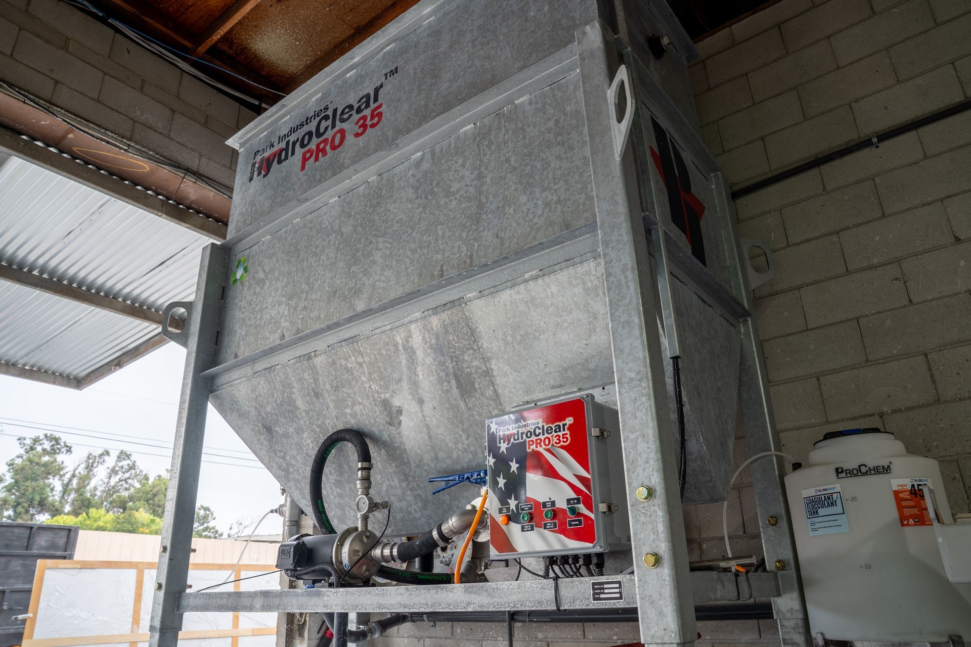 Large silver industrial machine in a warehouse, with red warning labels and piping on the front.