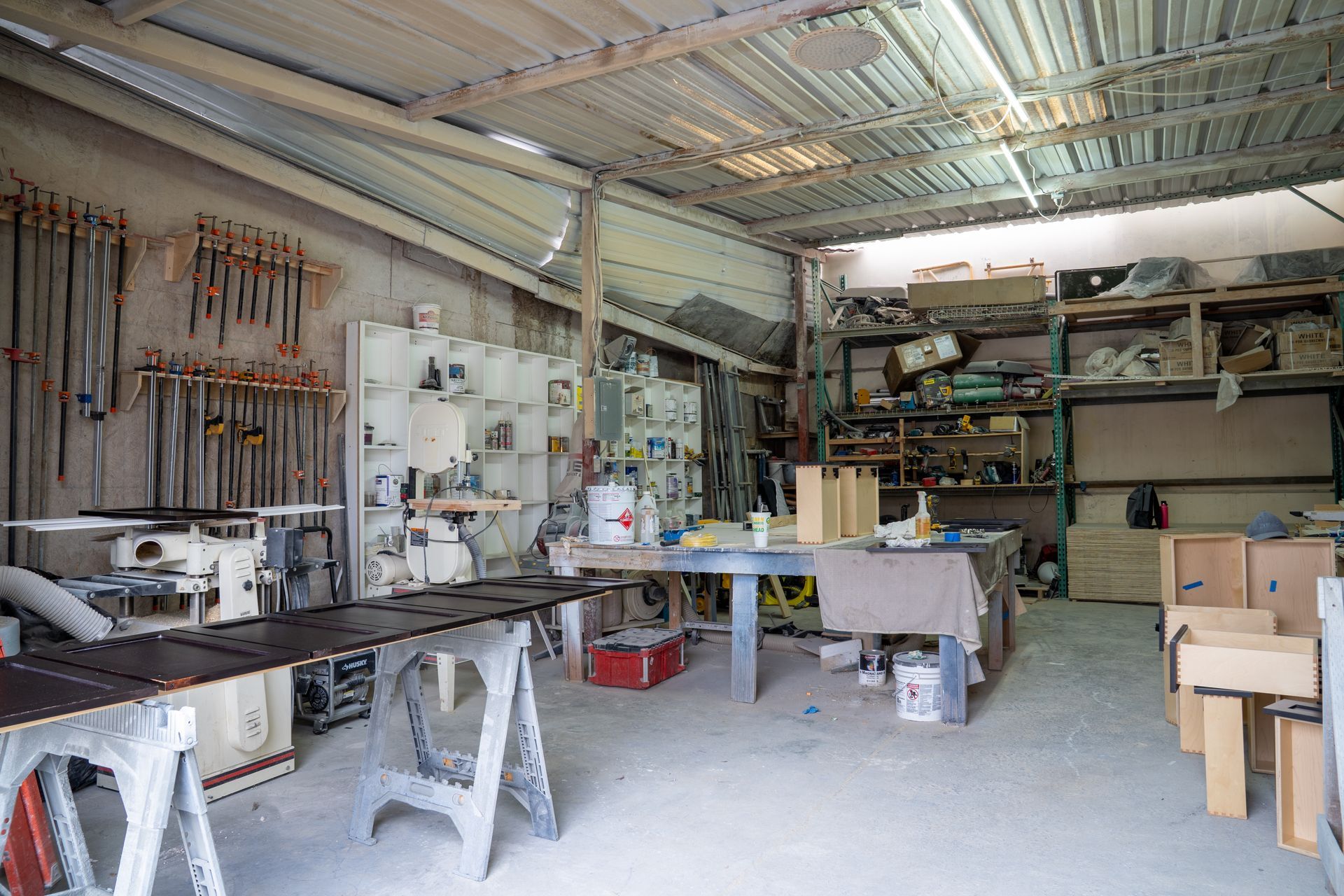 Cluttered workshop with tools, benches, shelves, and boxes under a corrugated metal roof