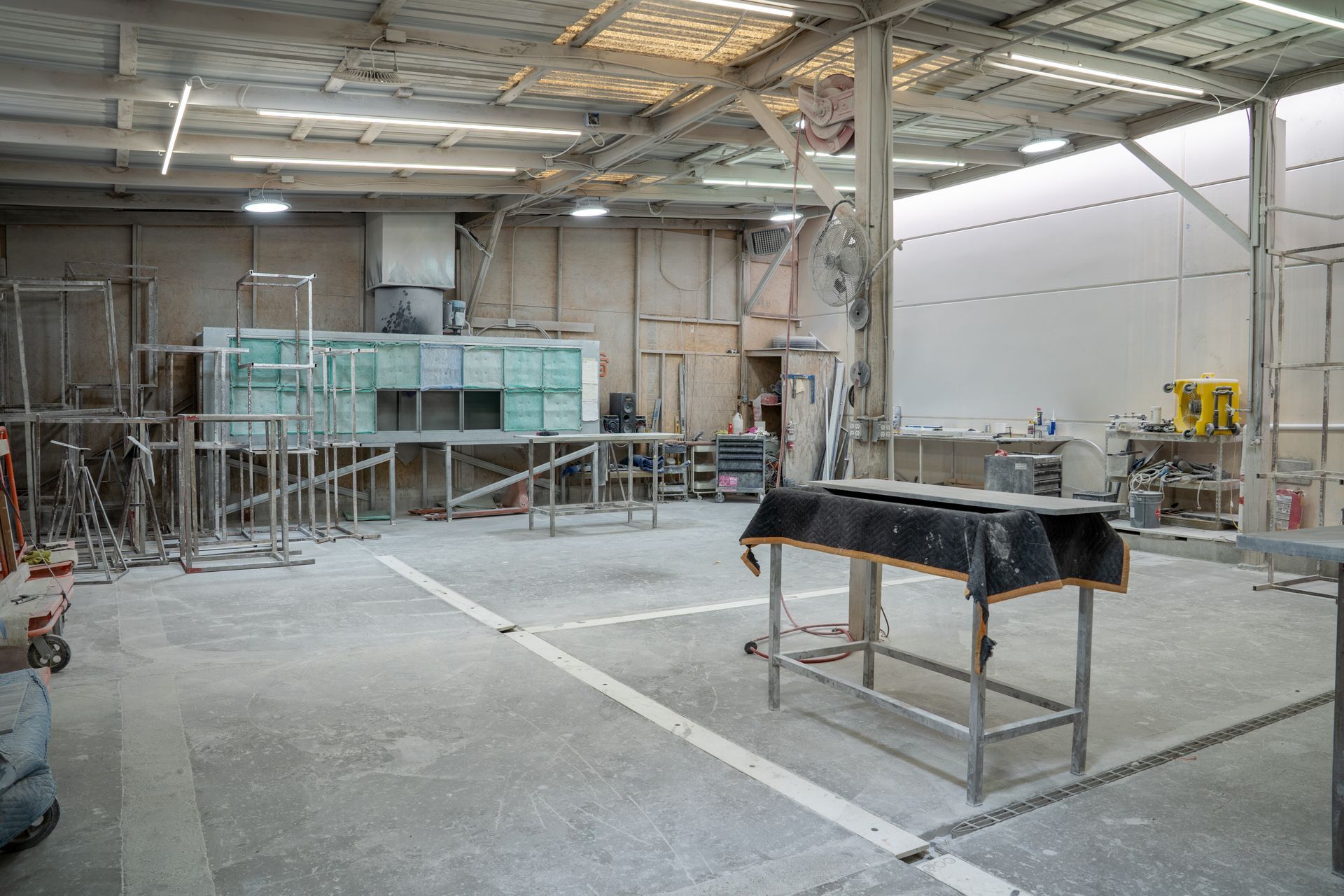 Interior of a dusty construction workshop with scaffolding, tools, and a table covered in black plastic.