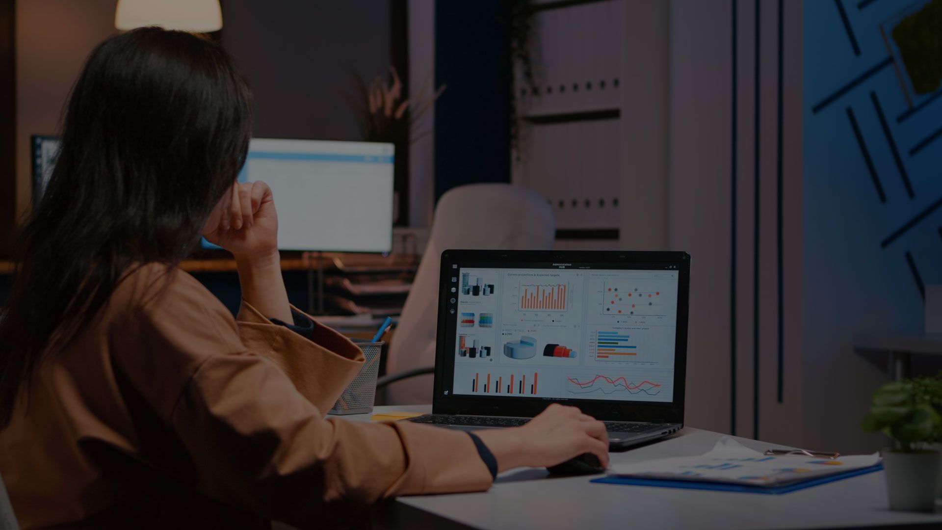 Woman working on laptop, viewing charts and graphs in office setting.