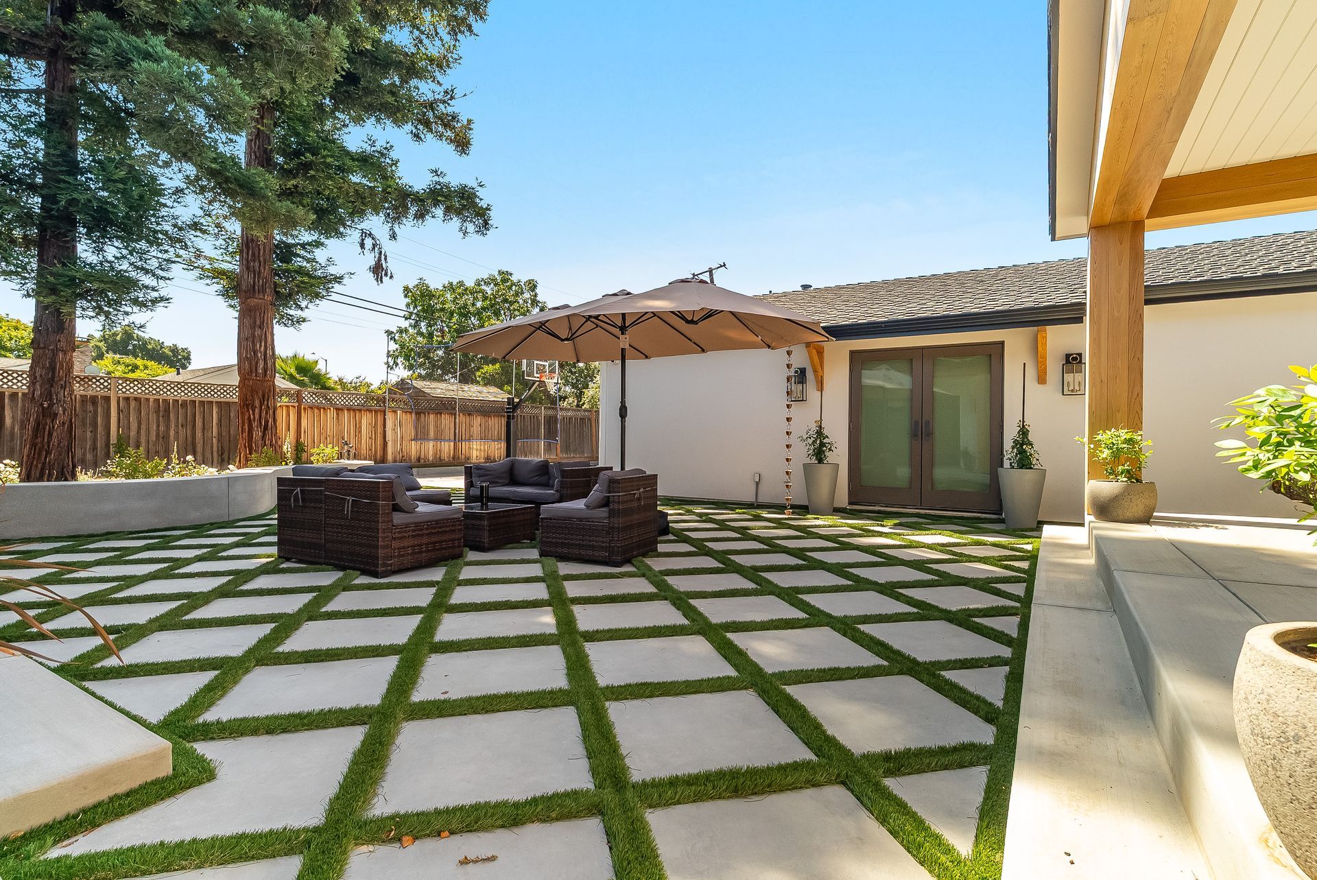 Modern backyard patio with stone grid lawn, wicker seating, umbrella, and sliding glass doors