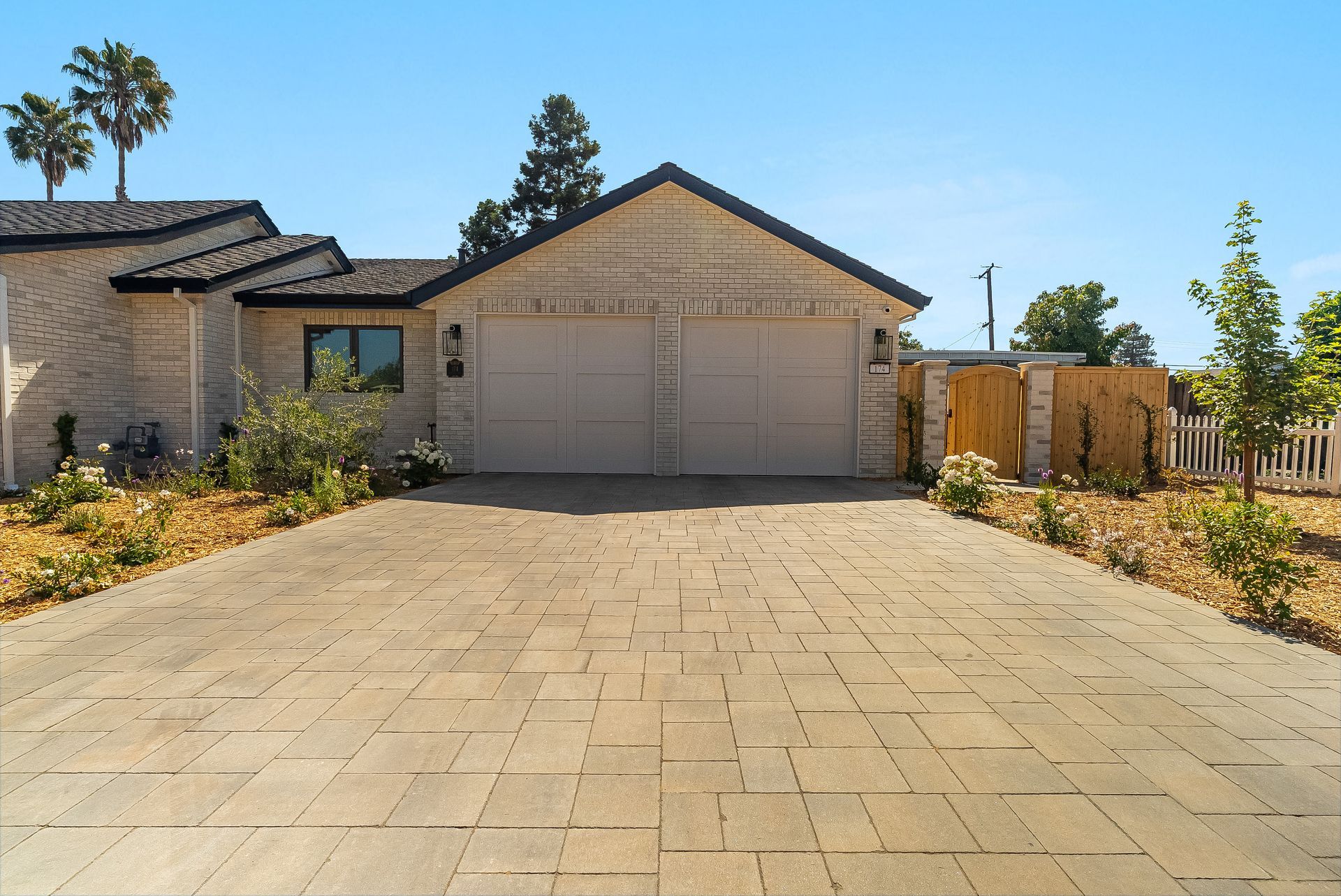 Single-story house with a two-car garage and a wide paved driveway under a clear blue sky