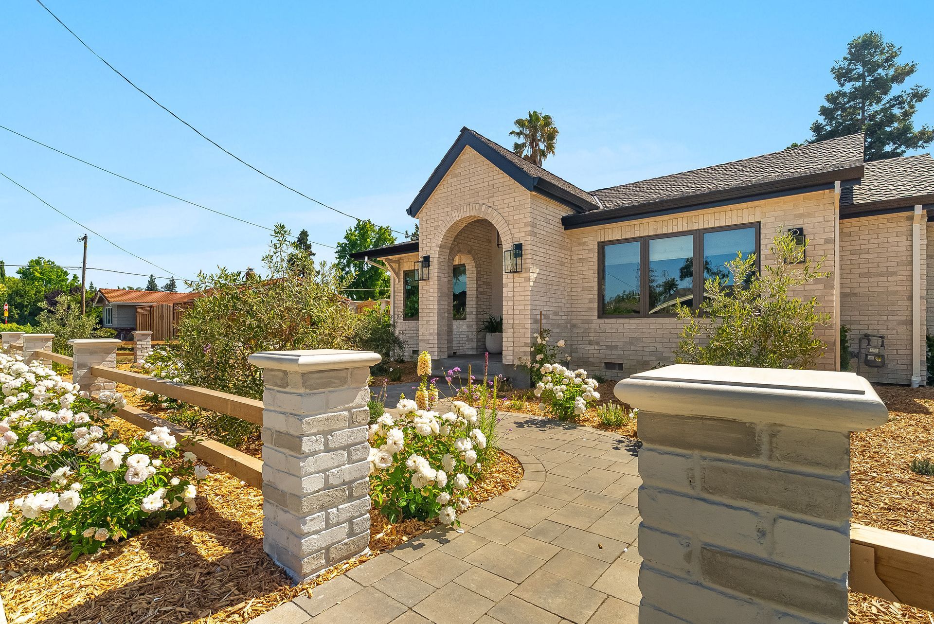 Brick house with arched entry, flower garden, and paved front walkway on a sunny day