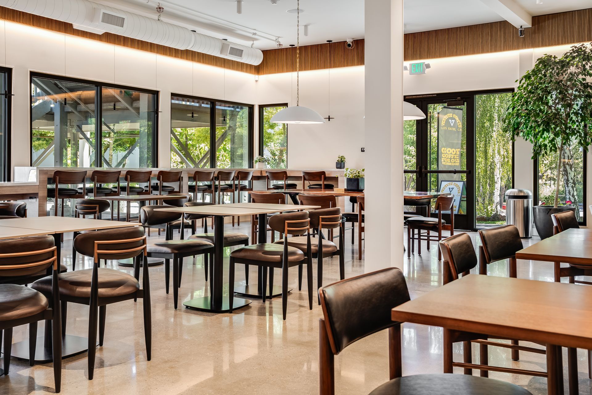 Modern café interior with wooden tables and chairs, large windows, and warm natural light