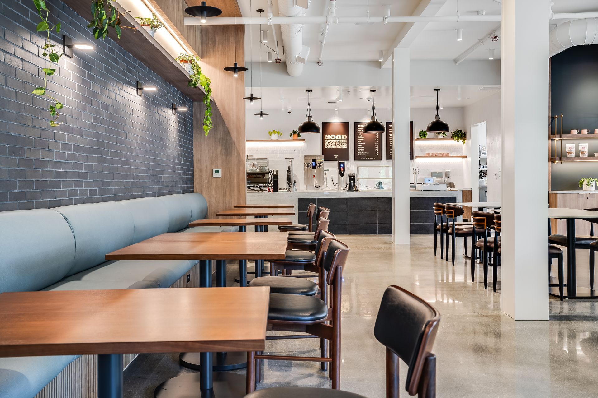 Modern cafe interior with wooden tables, black chairs, blue bench seating, and a bright open counter area