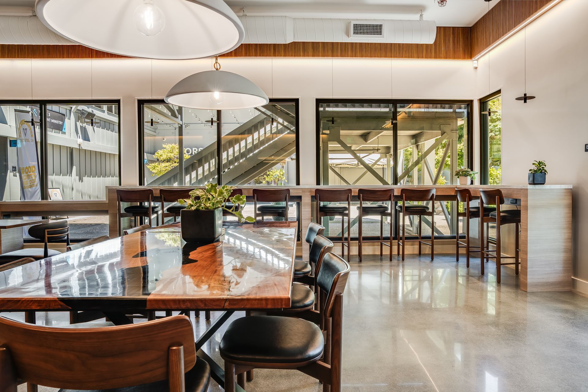 Modern café interior with wooden tables, large windows, and hanging pendant lights