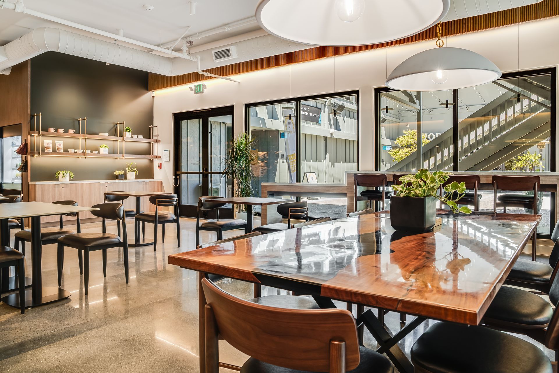 Modern cafe interior with wooden tables, black chairs, and large glass windows.