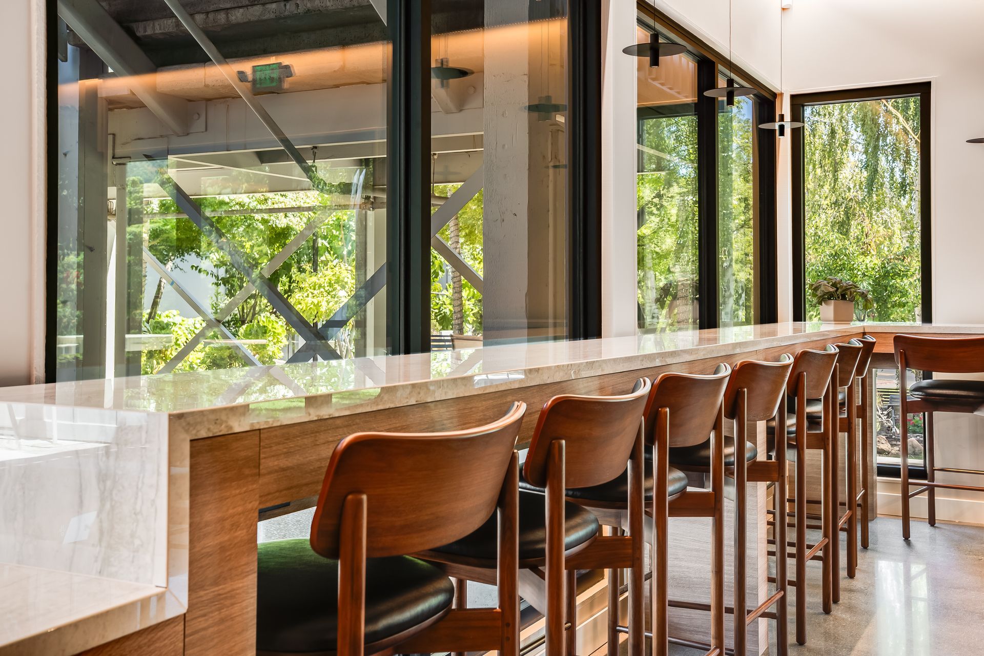 Modern dining room with wooden chairs and tables by large windows overlooking greenery