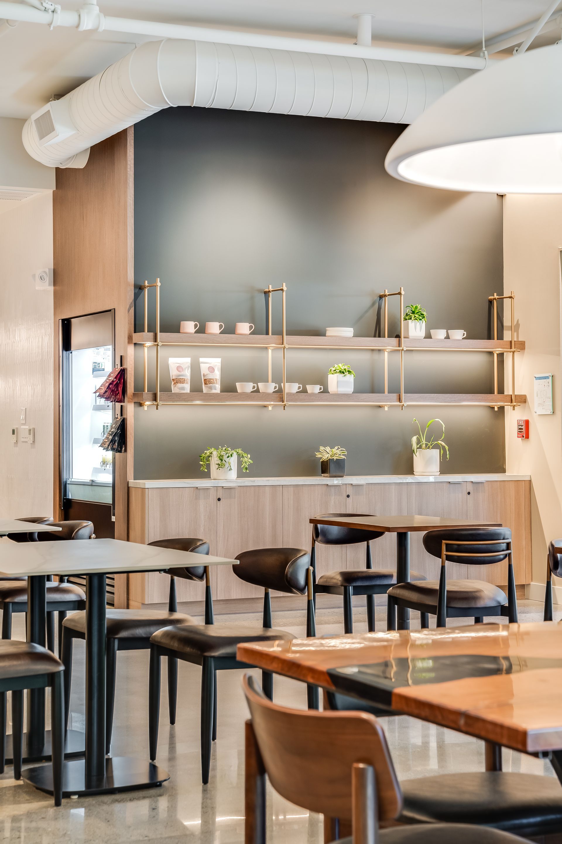 Modern cafe interior with wooden tables, black stools, shelves, and warm pendant lighting