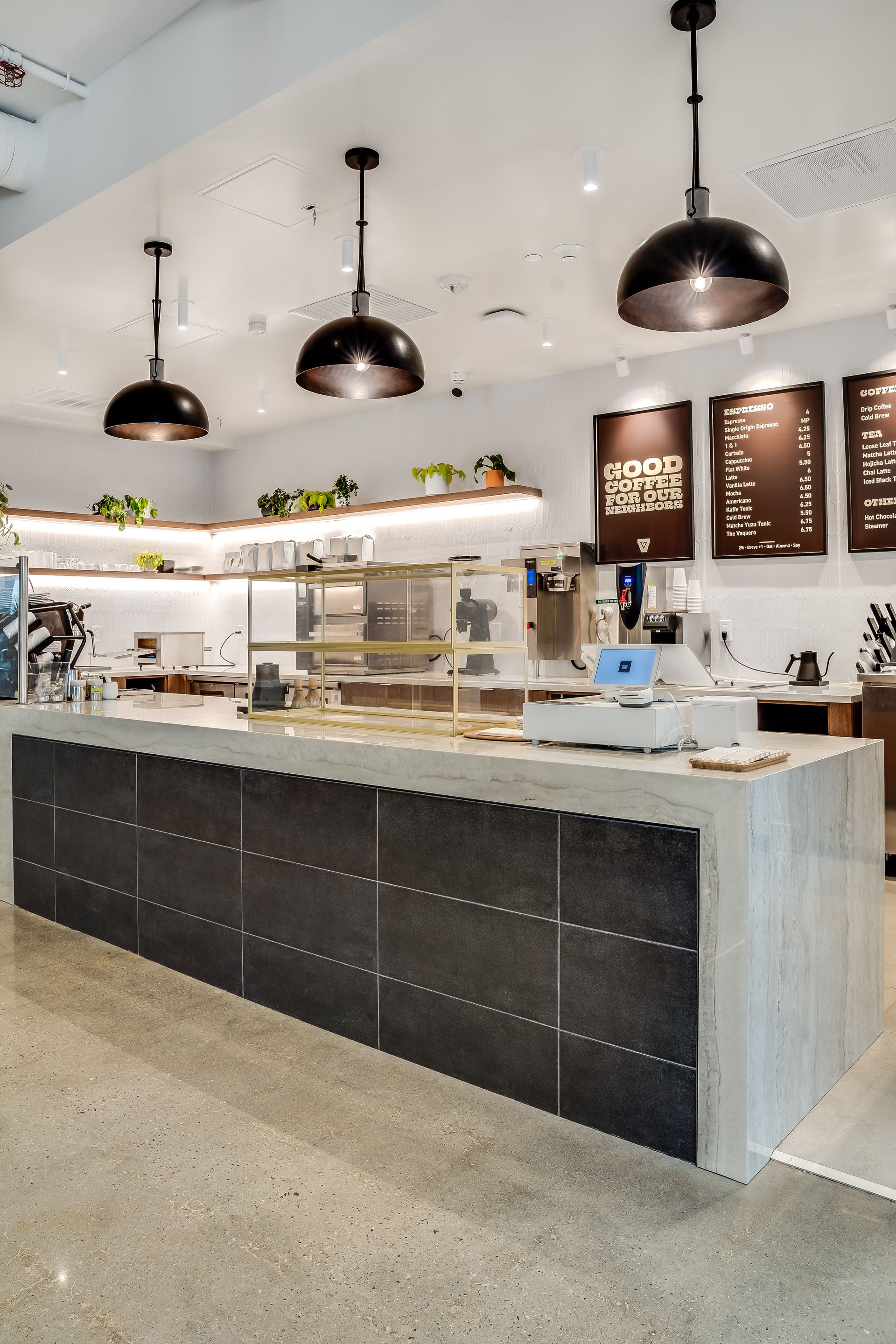 Bright modern café counter with pendant lights, marble top, and menu boards on a white wall