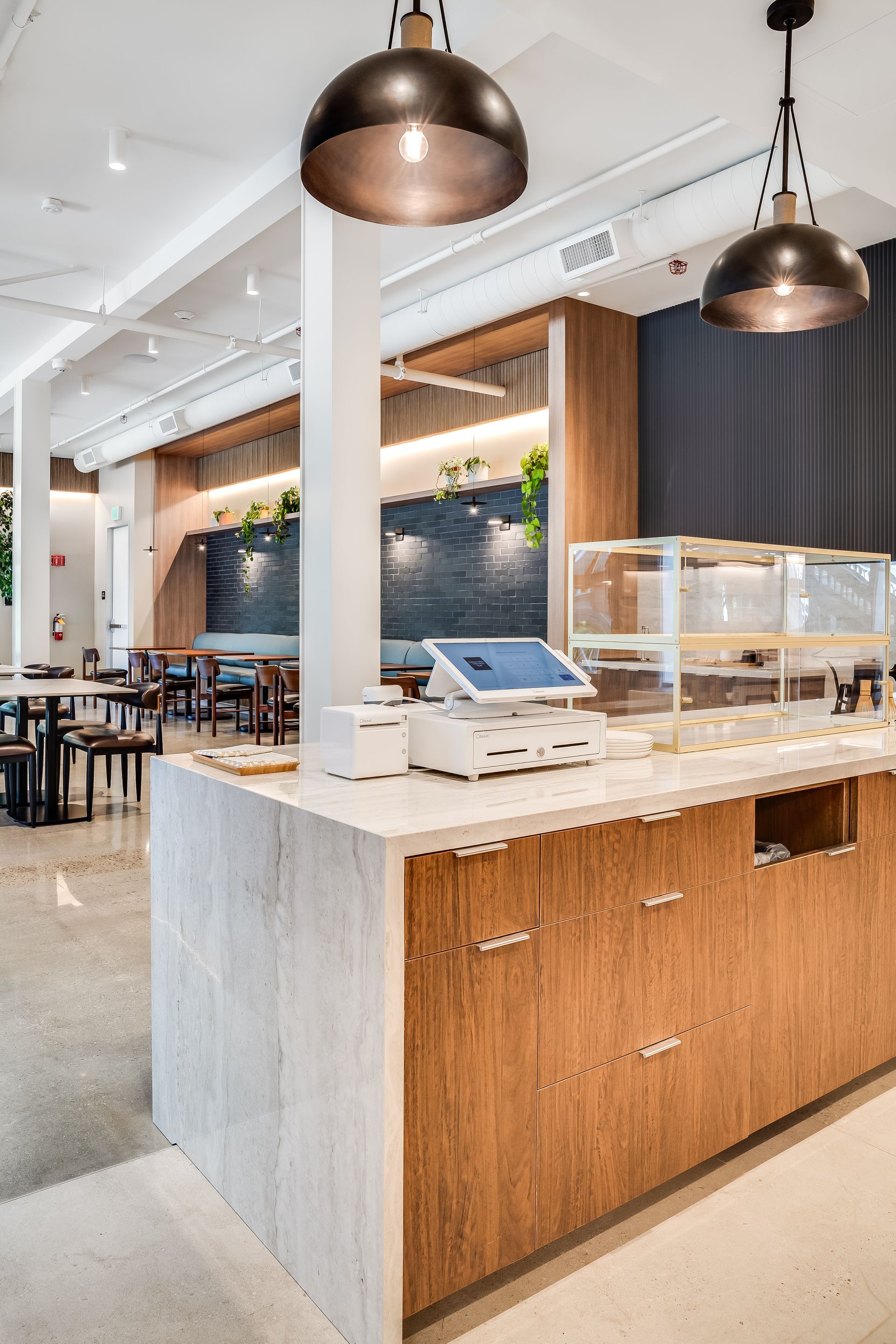 Modern café counter with wood panels, marble top, pendant lights, and a pastry display case