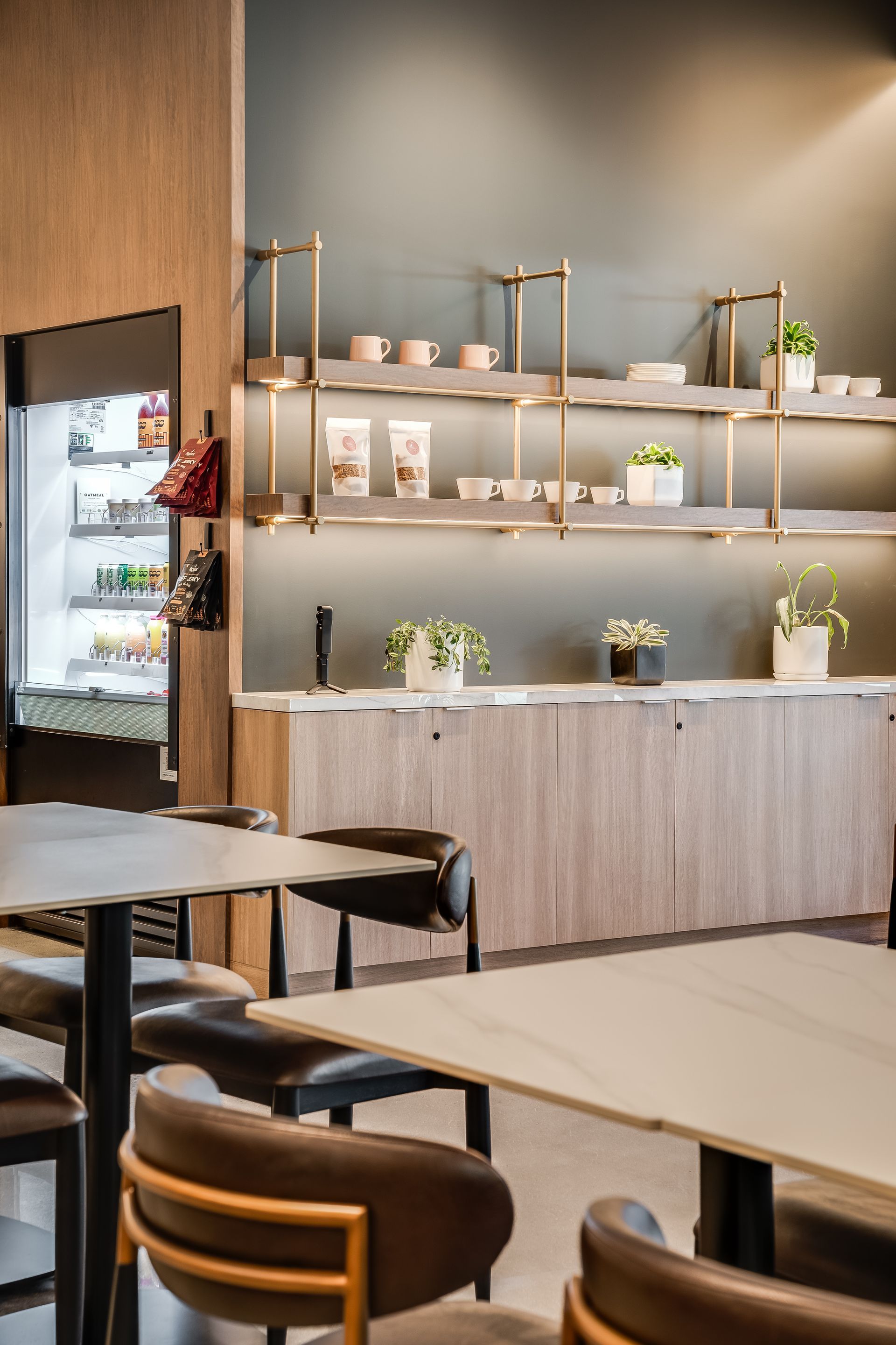 Modern café interior with wooden tables, wall shelves, and a refrigerated display case
