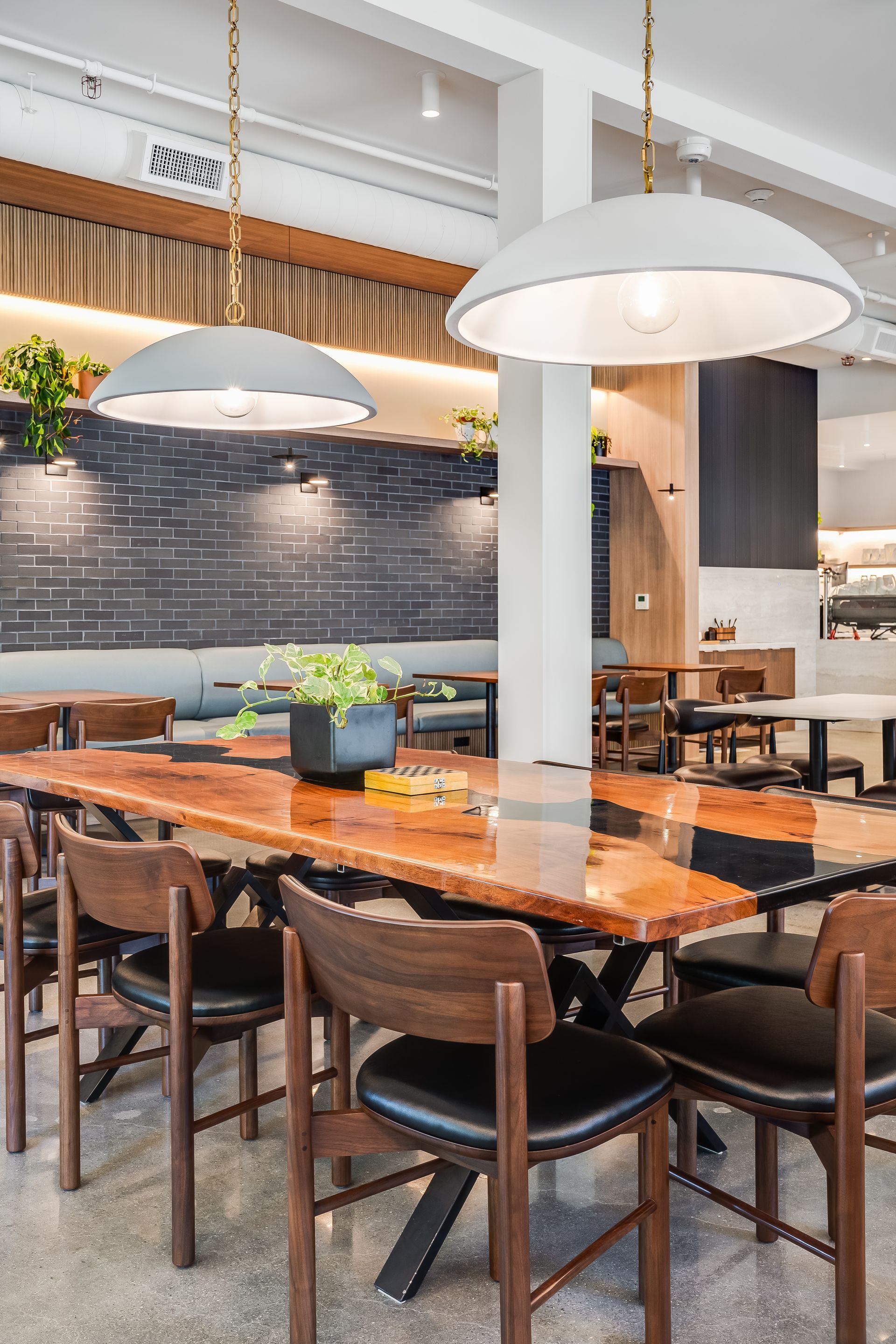 Modern dining area with wooden tables, brown chairs, pendant lights, and a gray tile wall