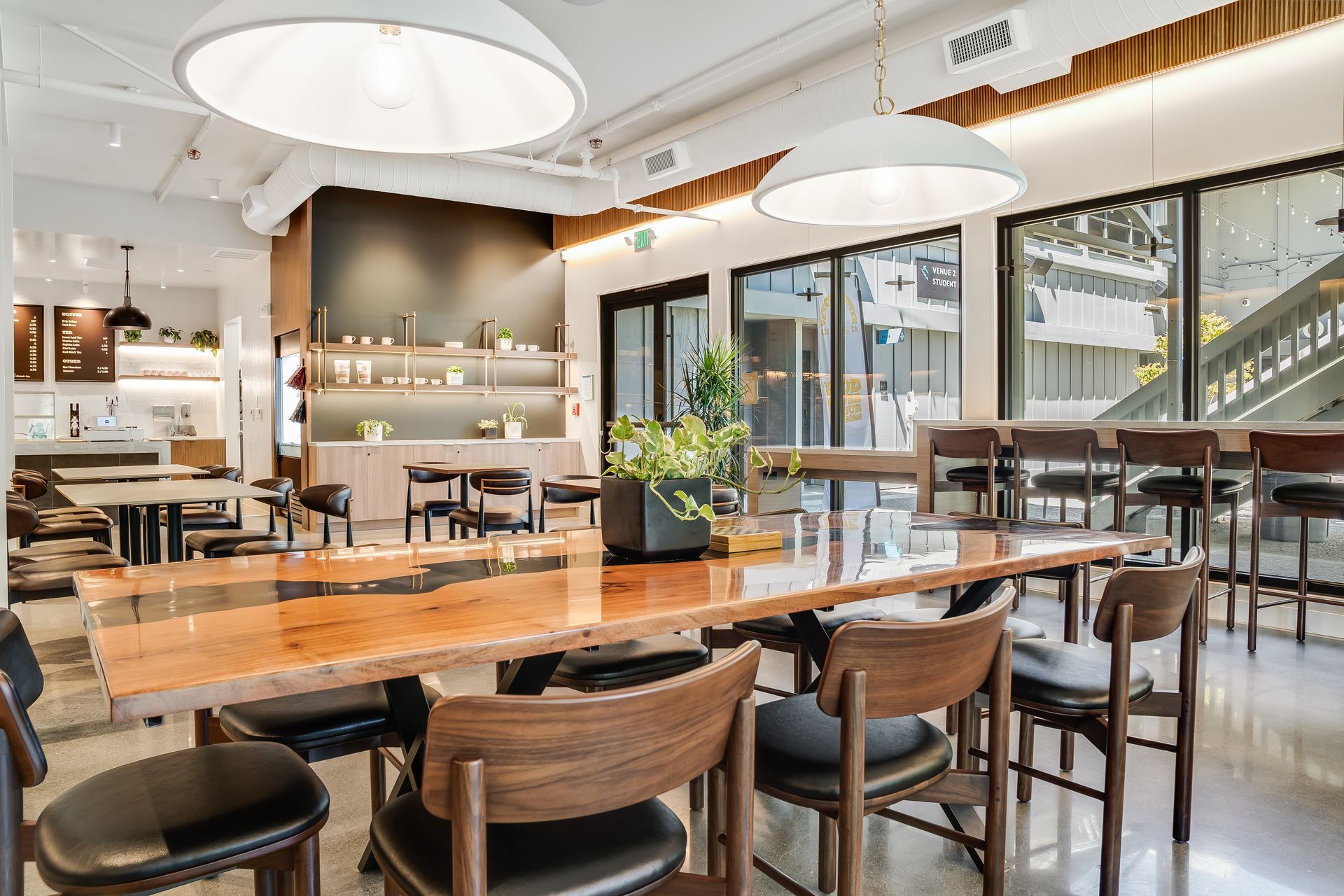 Bright modern restaurant interior with wooden tables, bar seating, and large windows overlooking a patio