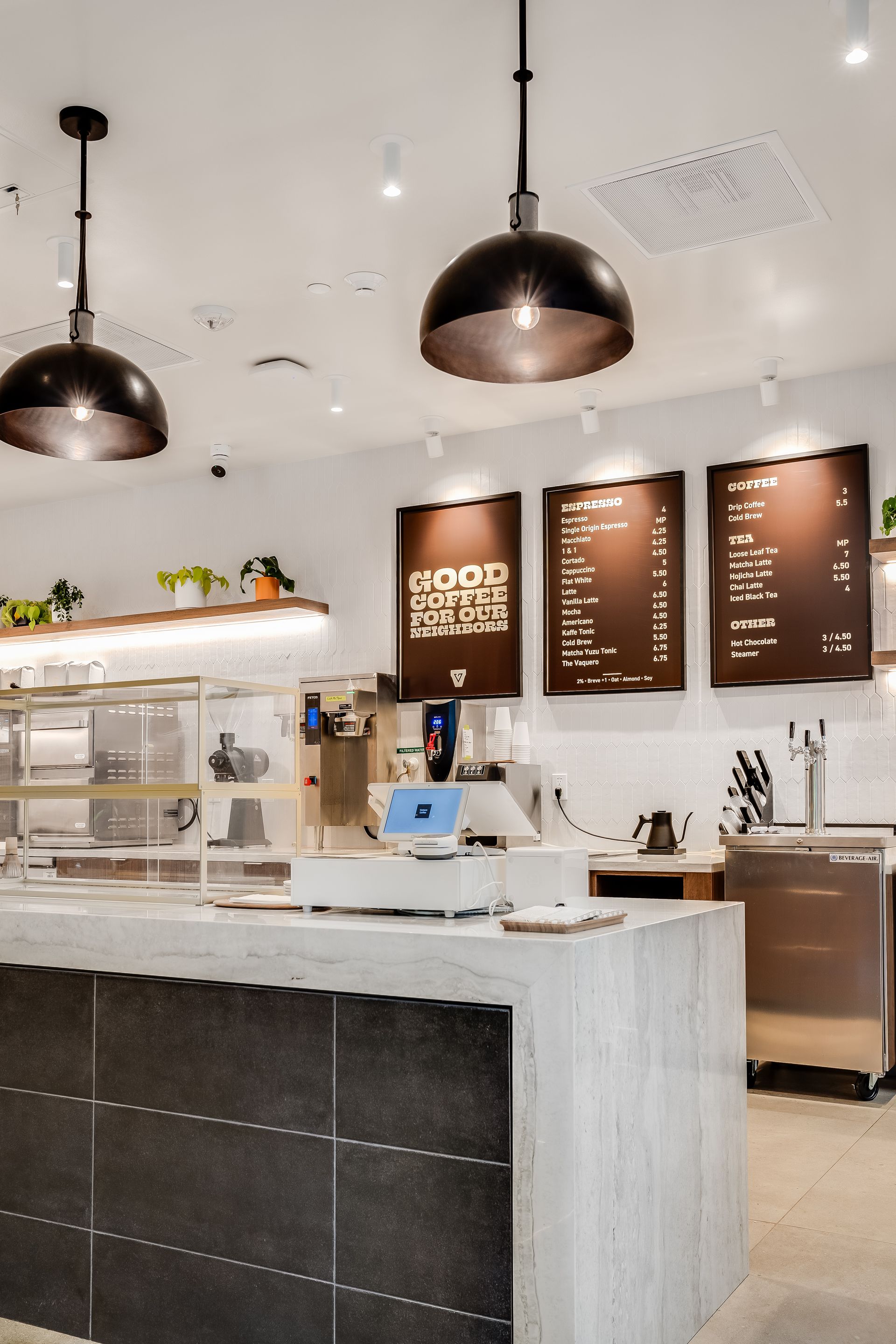 Modern café counter with pastries, coffee equipment, and menu boards under black pendant lights