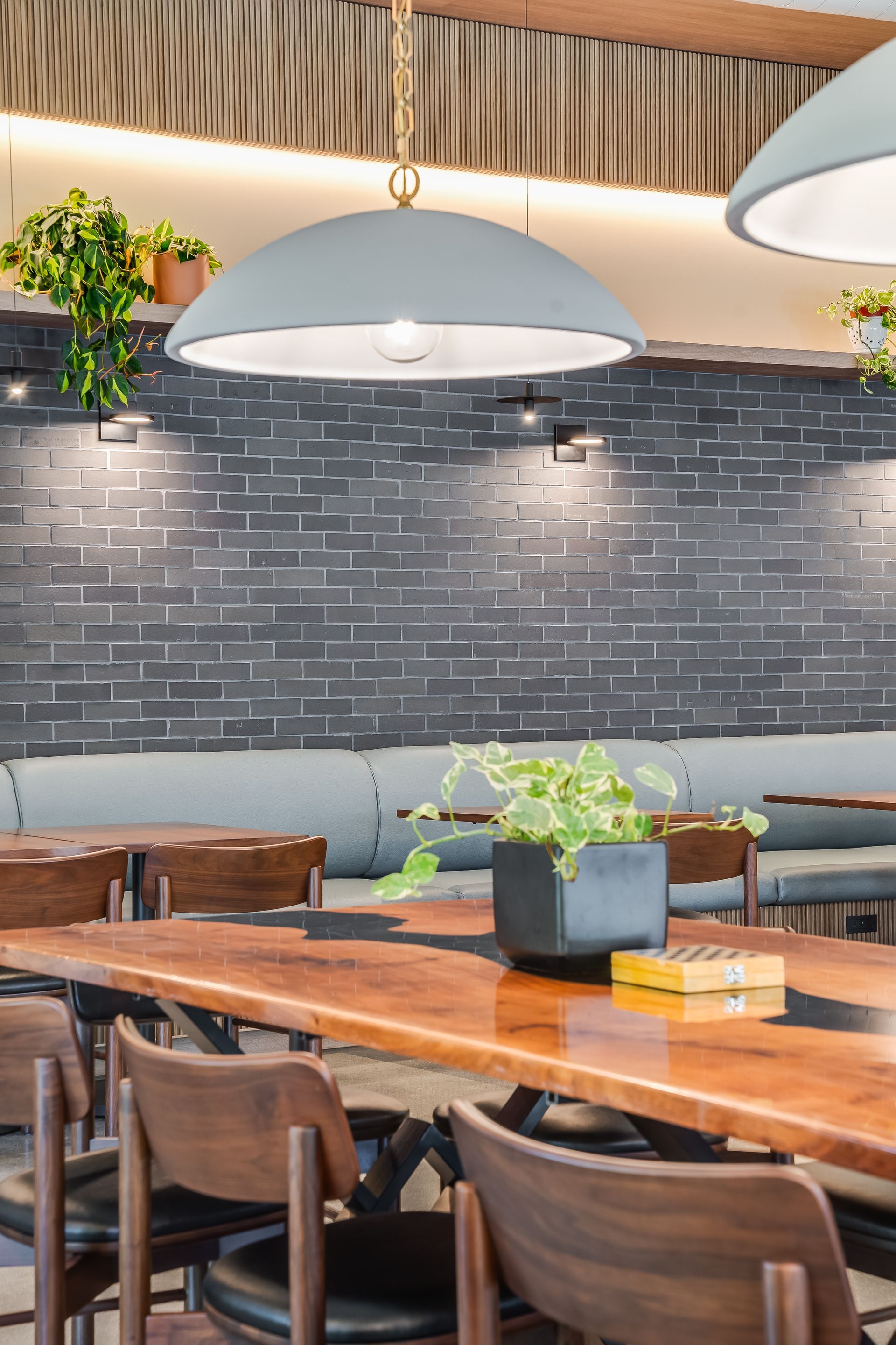 Modern café interior with wooden tables, brown chairs, gray brick wall, and hanging dome lights