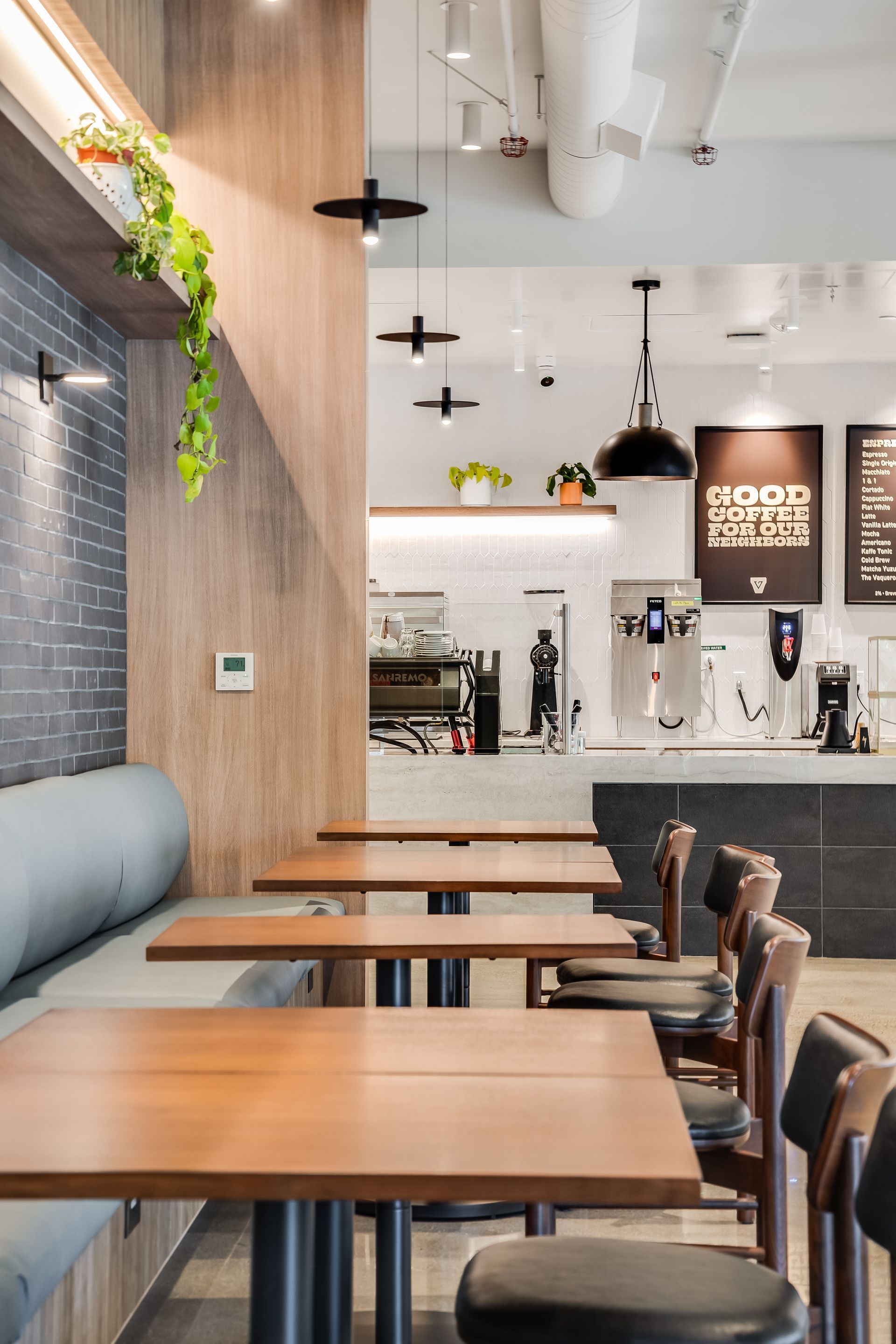 Modern café interior with wooden tables, black chairs, hanging lights, and a coffee counter in back