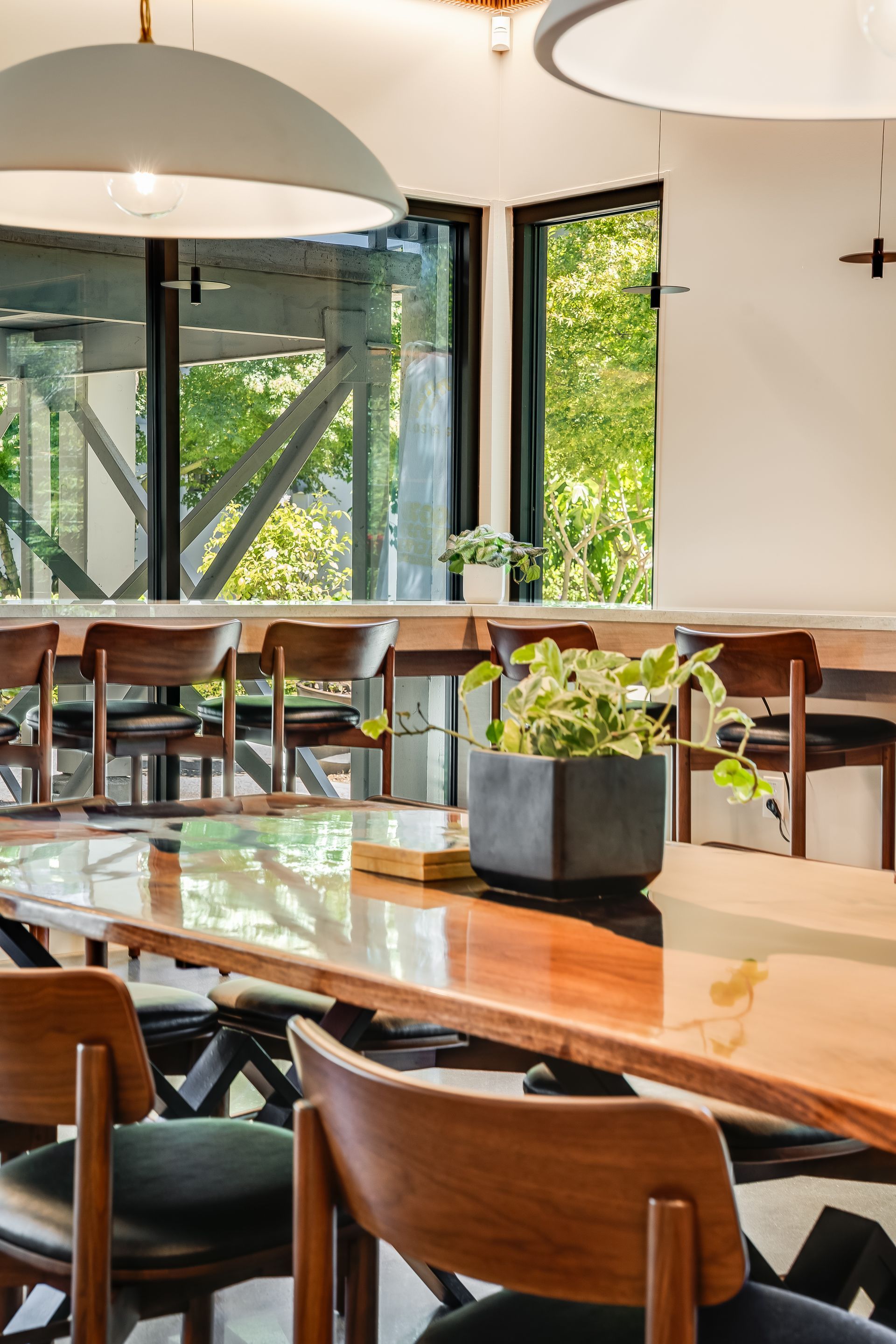 Bright cafe interior with wooden tables, hanging lamps, and green plants by large windows