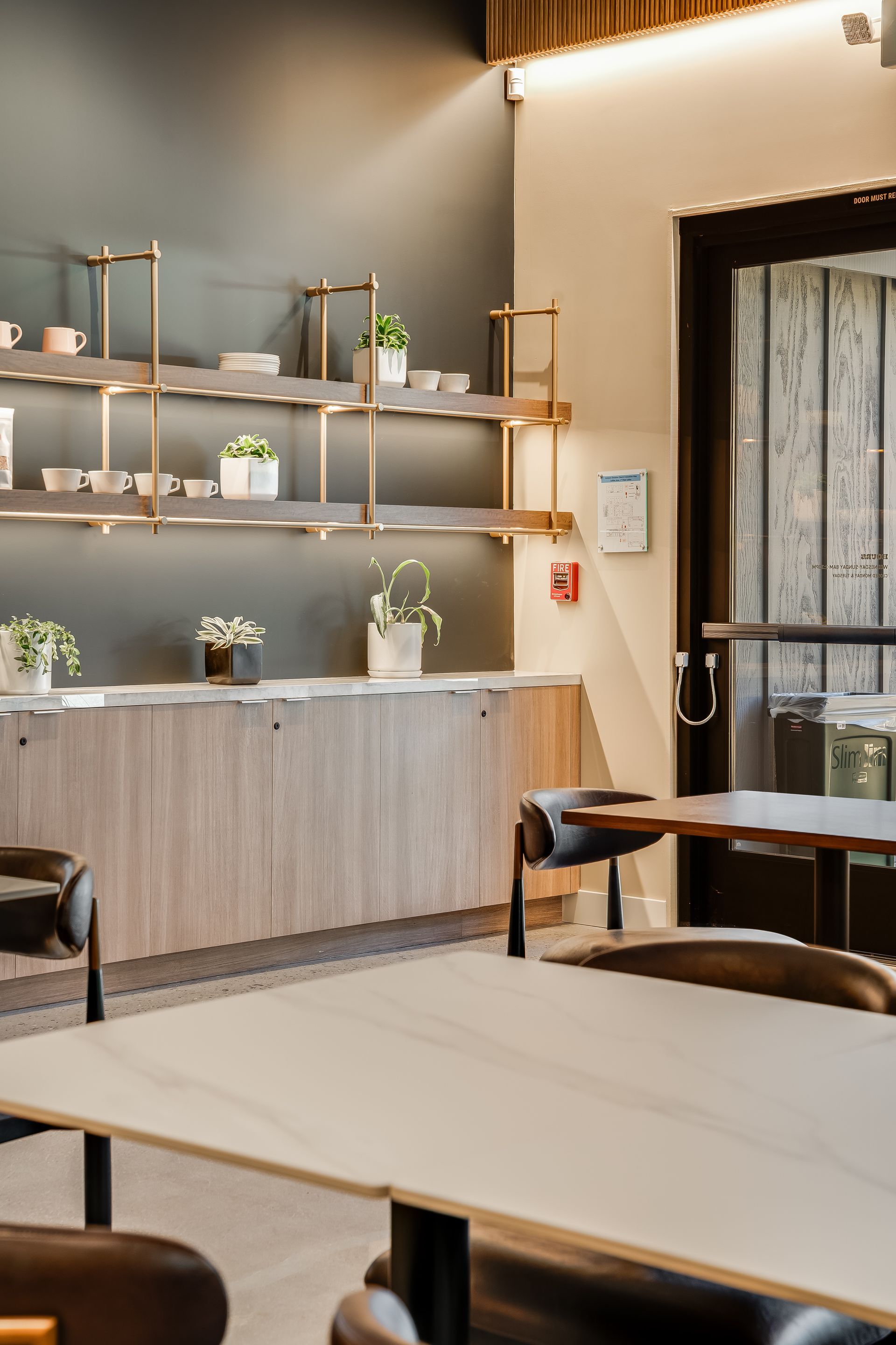 Modern café interior with shelves, plants, and wooden tables by a window