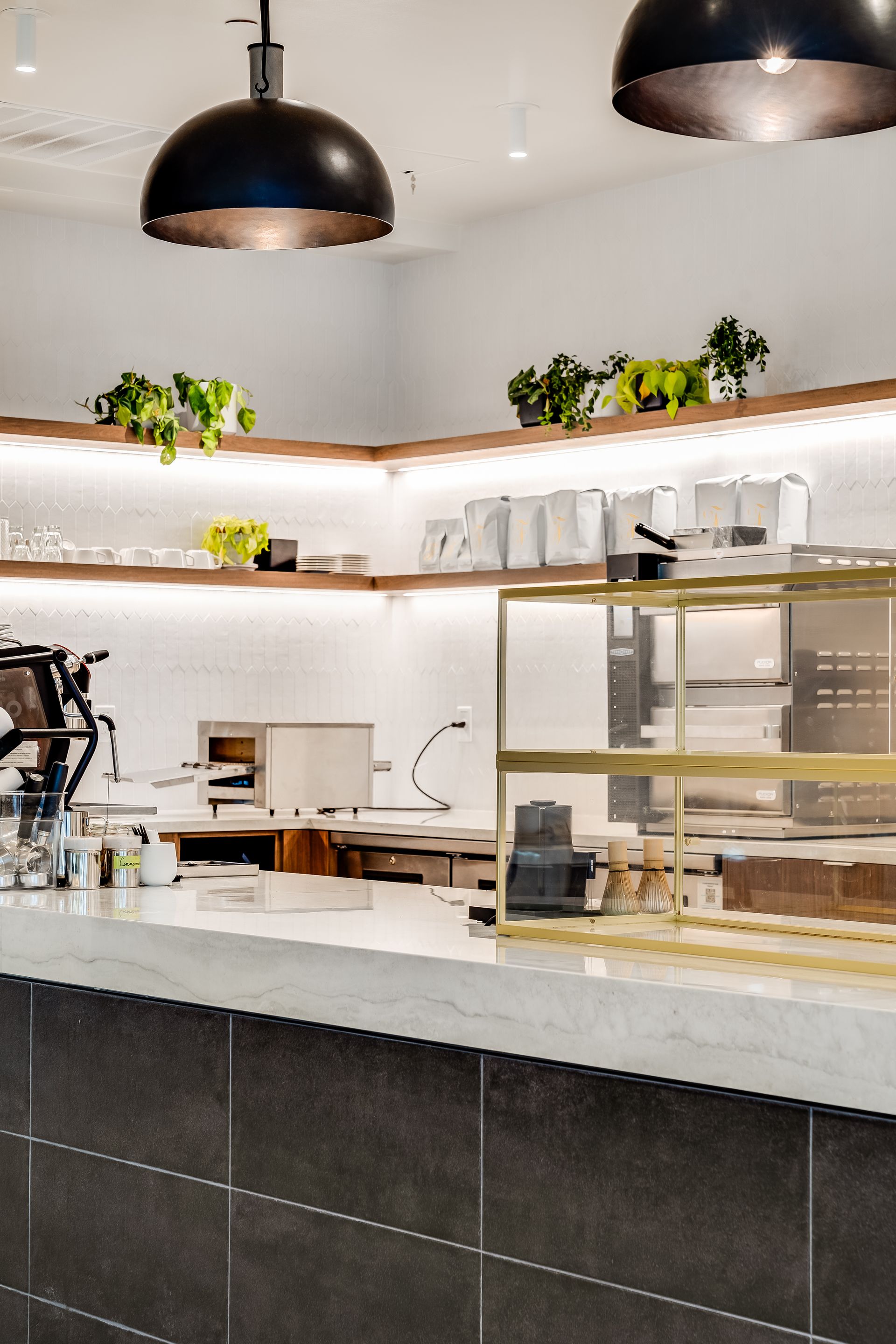 Modern café interior with white shelves, plants, warm lighting, and a marble-front counter