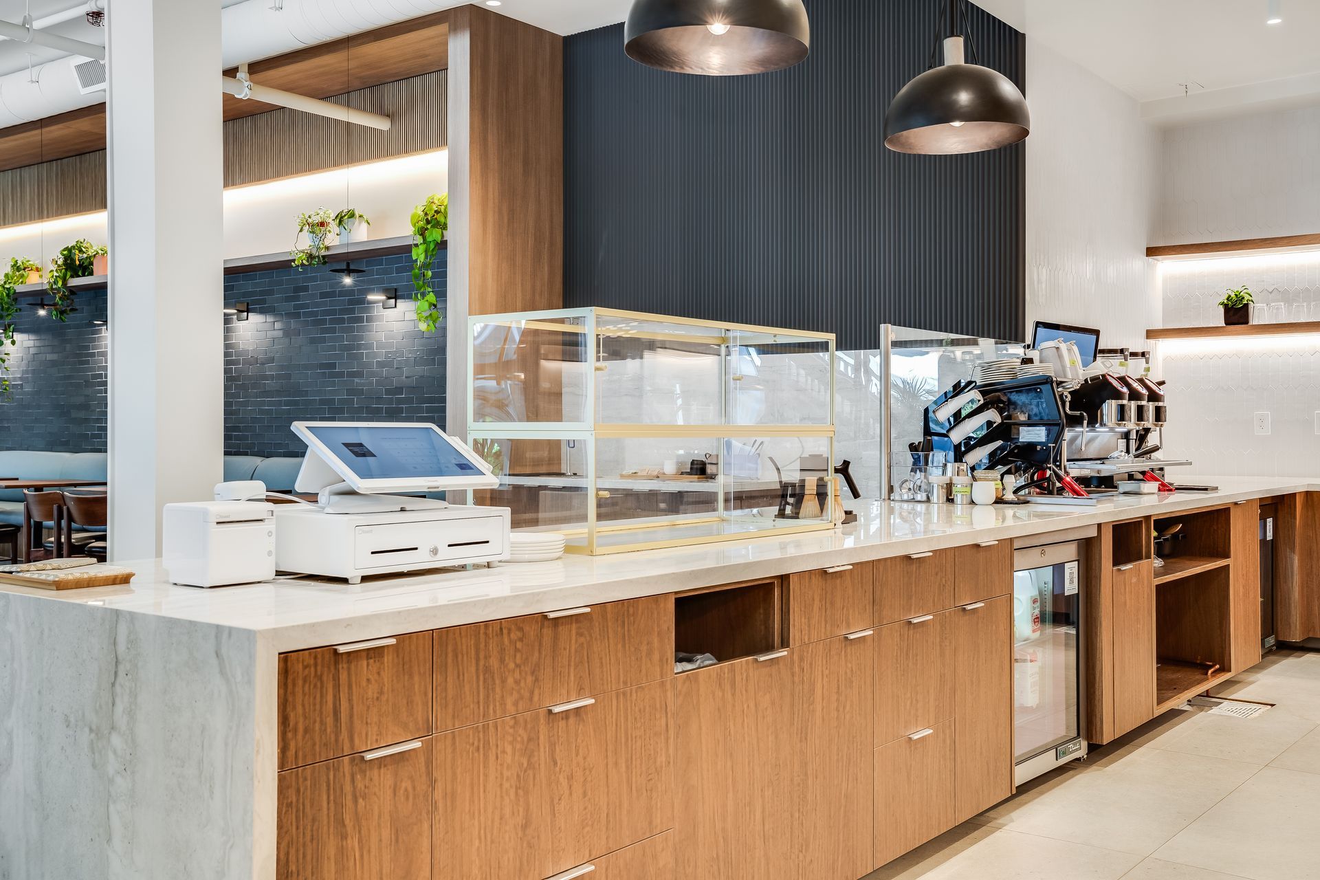 Modern cafe counter with wood cabinets, white marble top, glass display case, and pendant lights