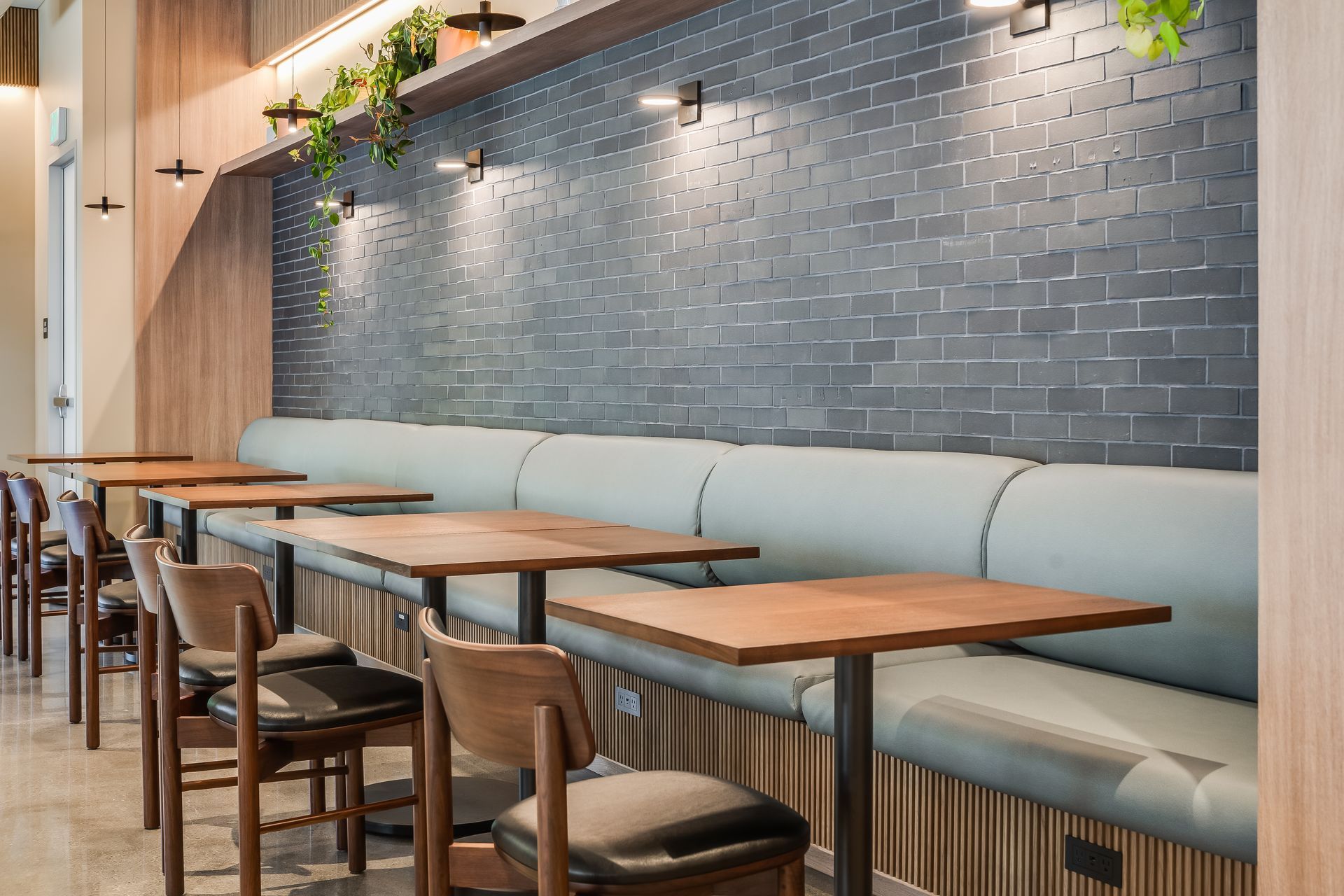 Empty café seating with wooden tables, chairs, and a light blue banquette along a gray tiled wall
