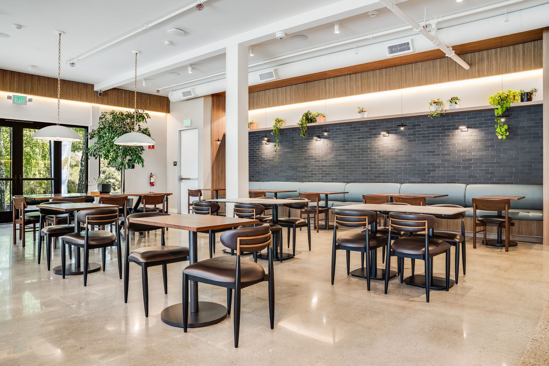 Modern café dining room with wooden tables, black chairs, hanging lights, and a large chalkboard wall