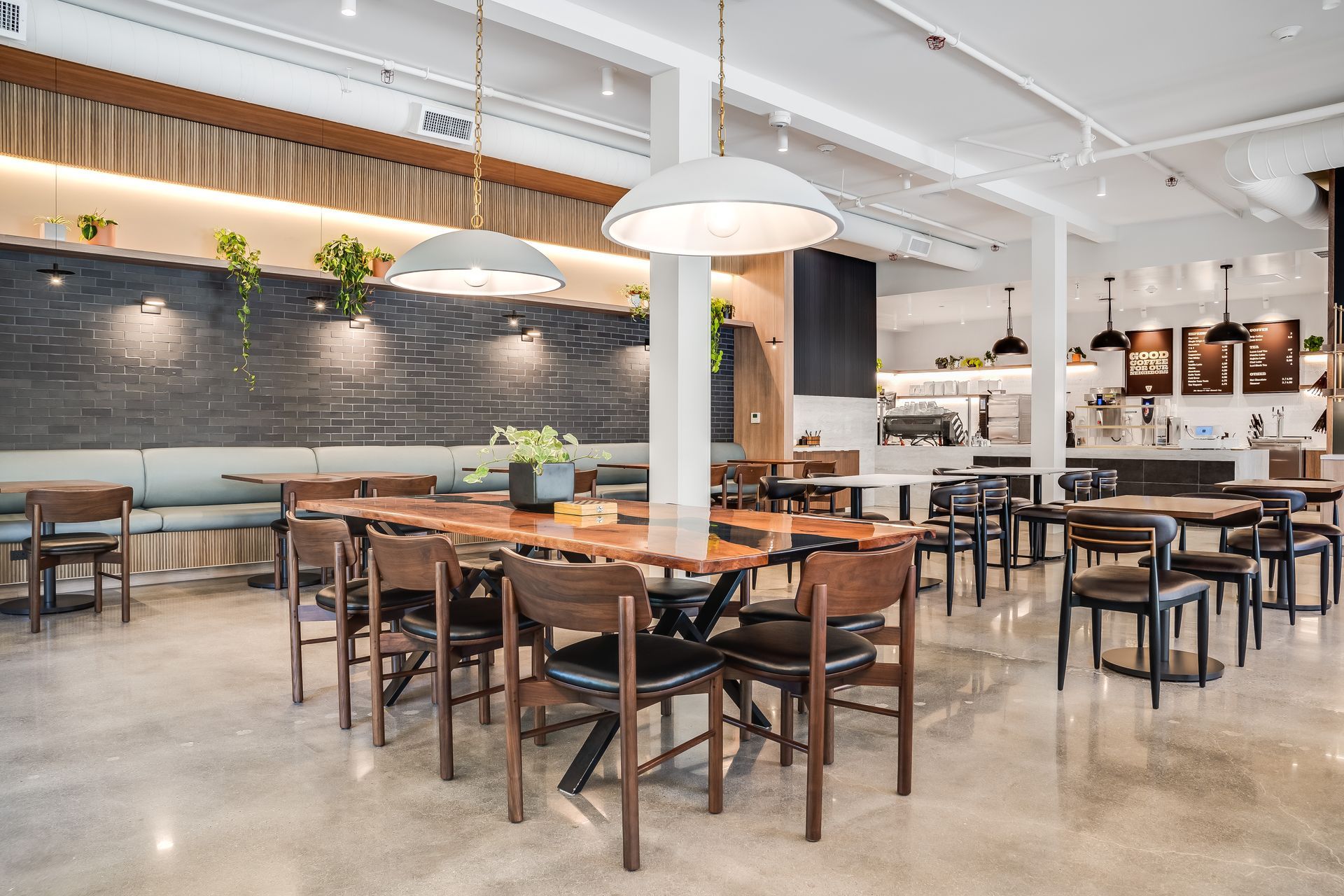 Modern restaurant dining area with wooden tables, black chairs, and warm pendant lighting