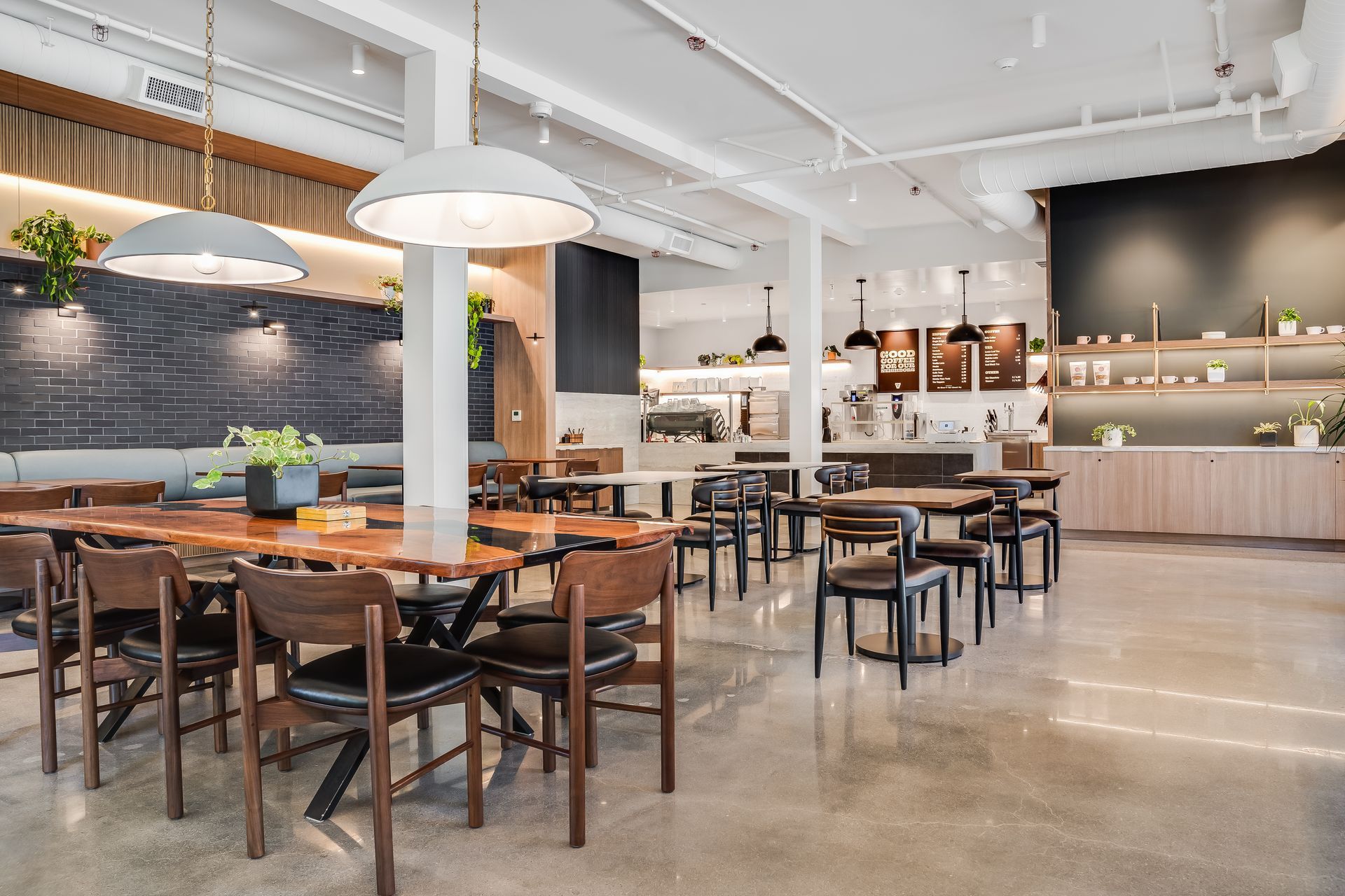 Modern restaurant dining area with wooden tables, black chairs, and a light wood bar under pendant lights