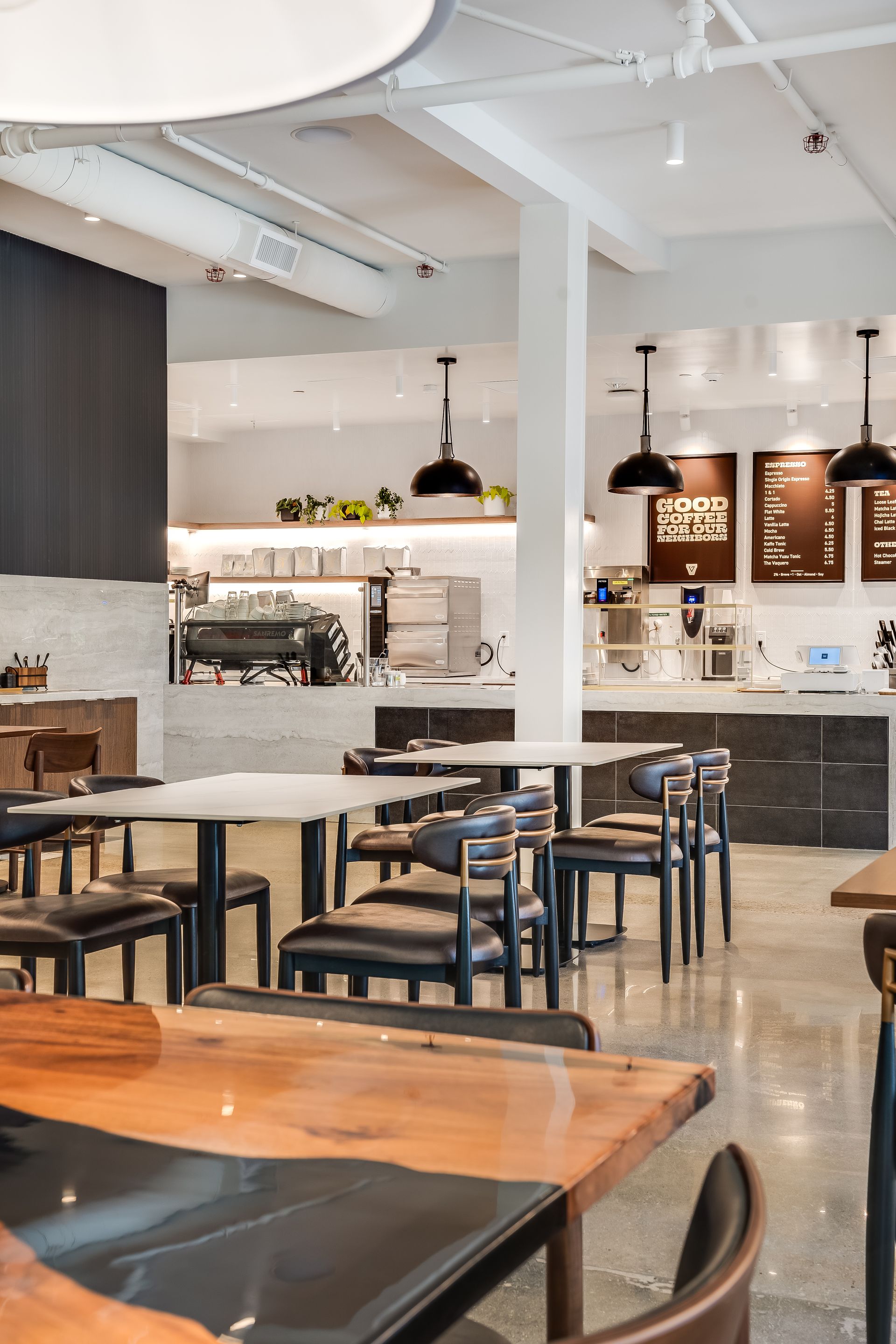 Modern café interior with wooden tables, black chairs, pendant lights, and a bar counter