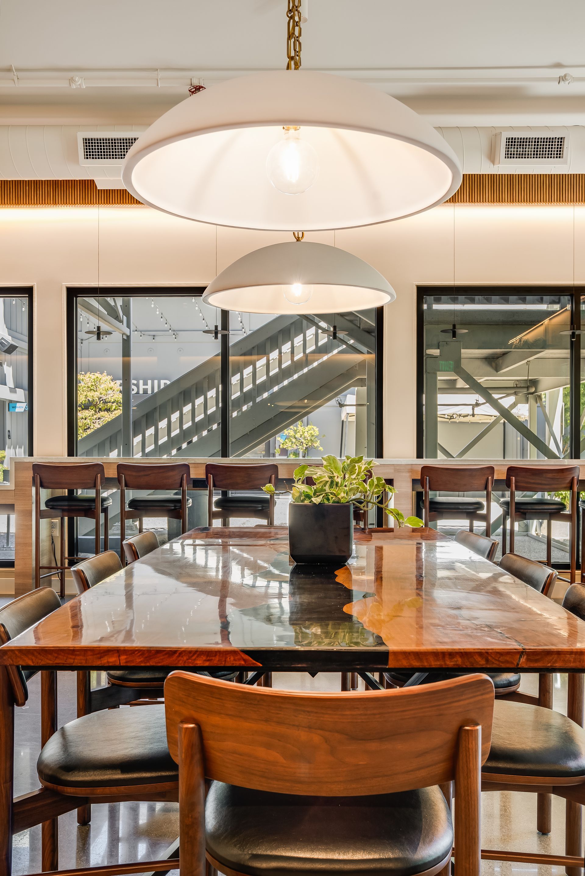 Modern cafe interior with wooden tables, pendant lights, and large windows looking onto a staircase outside