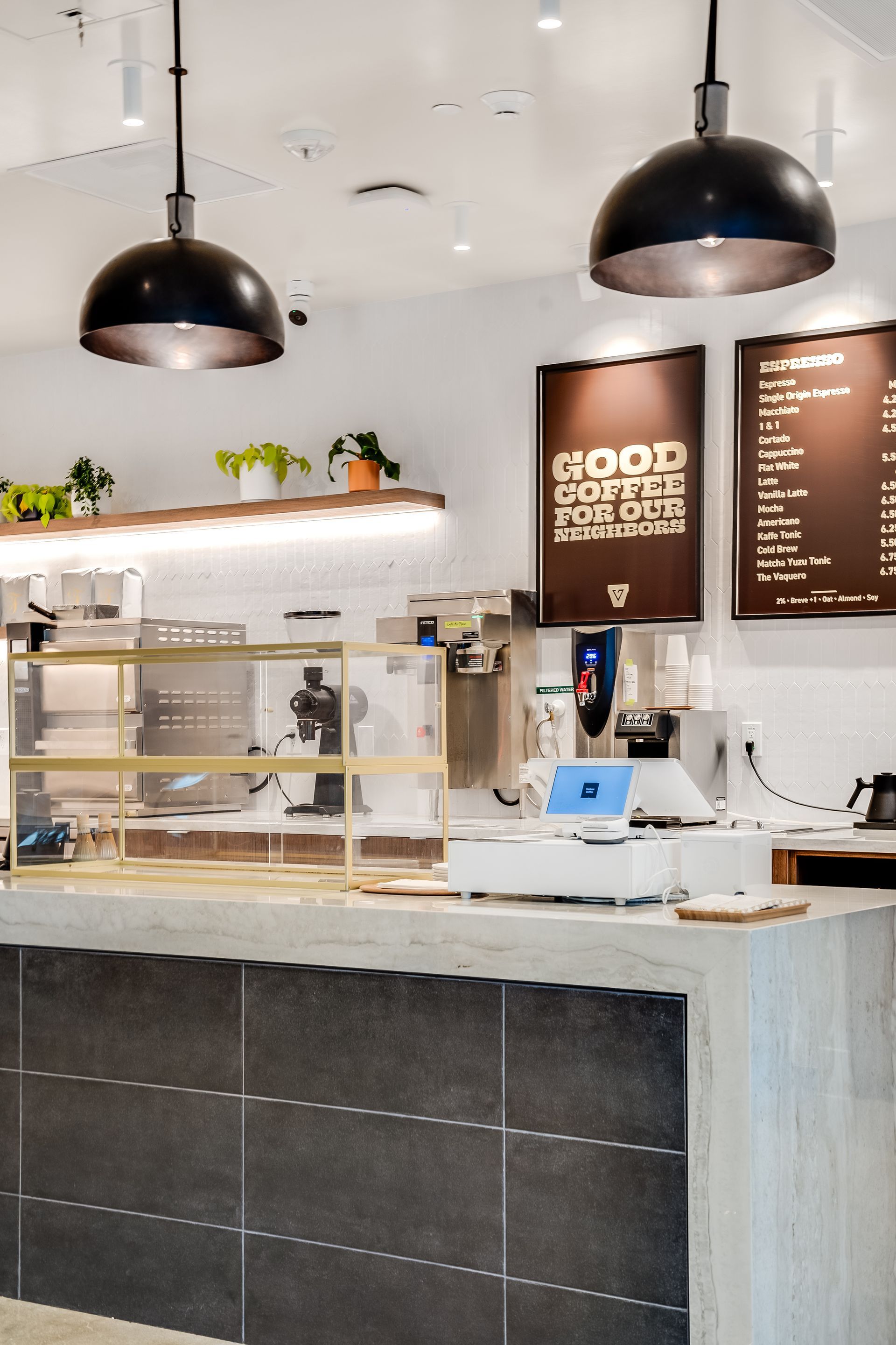 Modern coffee shop counter with glass pastry case, menu boards, and hanging black pendant lights