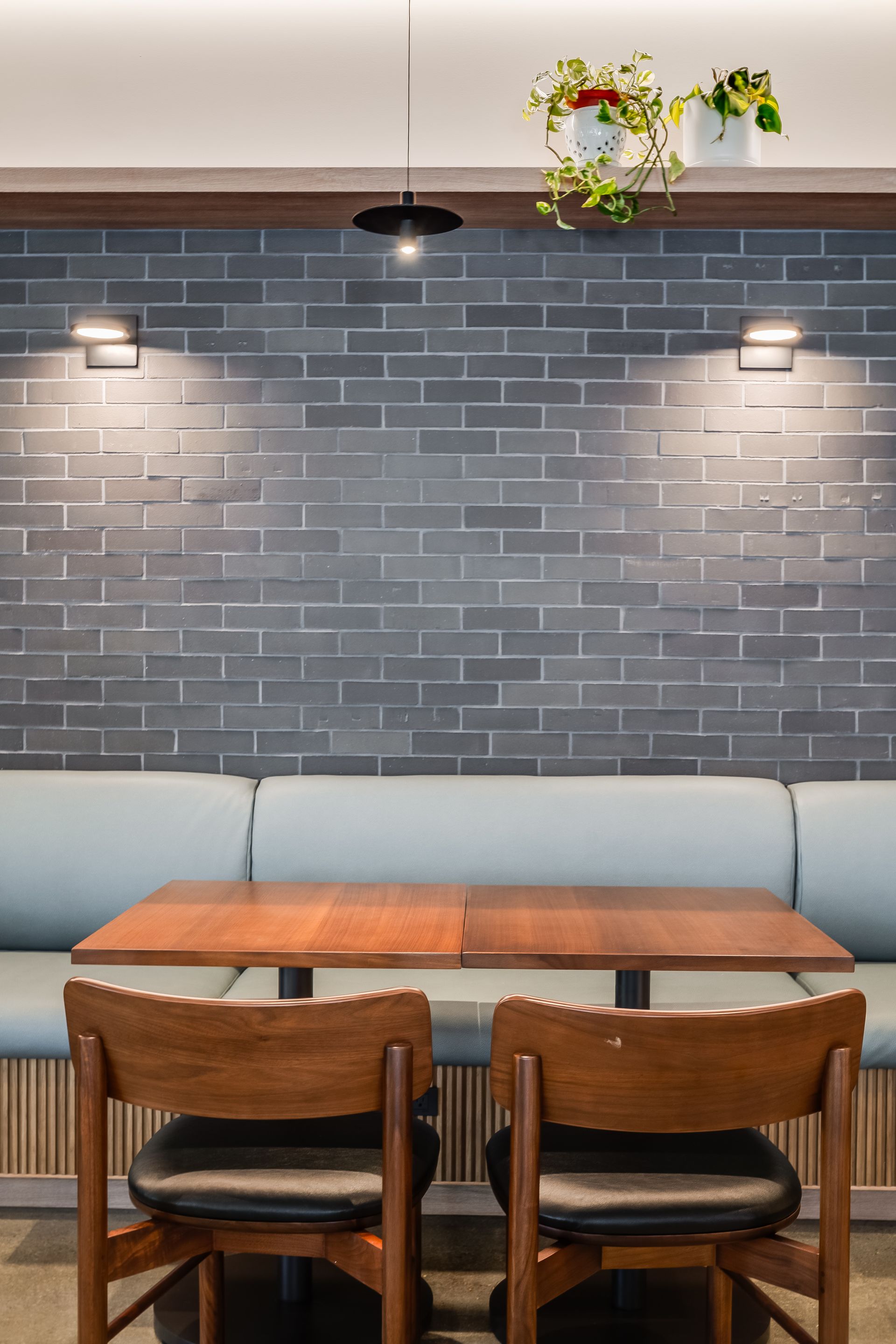 Cozy cafe booth with wooden tables and chairs, pale blue seating, and a gray brick accent wall with hanging plants.