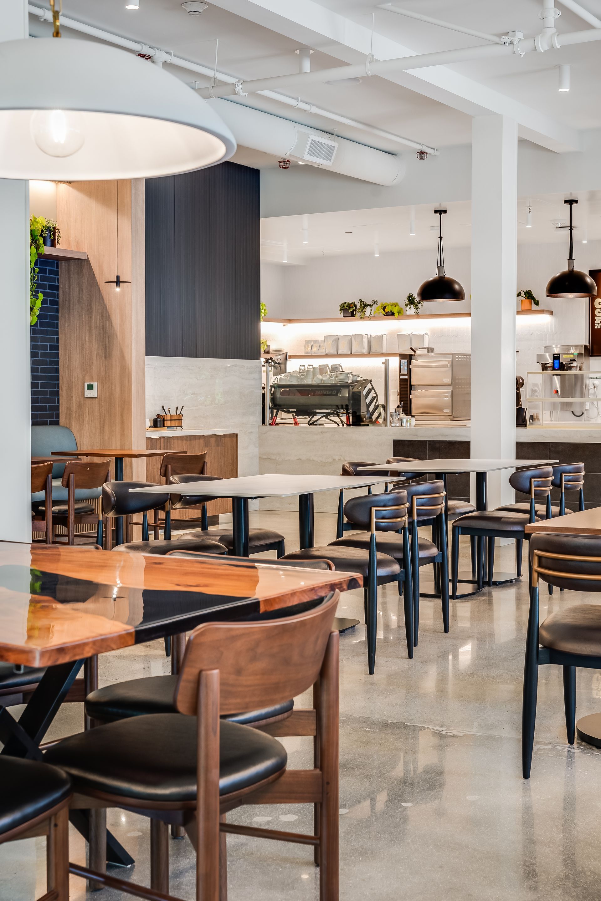 Modern café interior with wooden tables, black chairs, and a bright open counter area