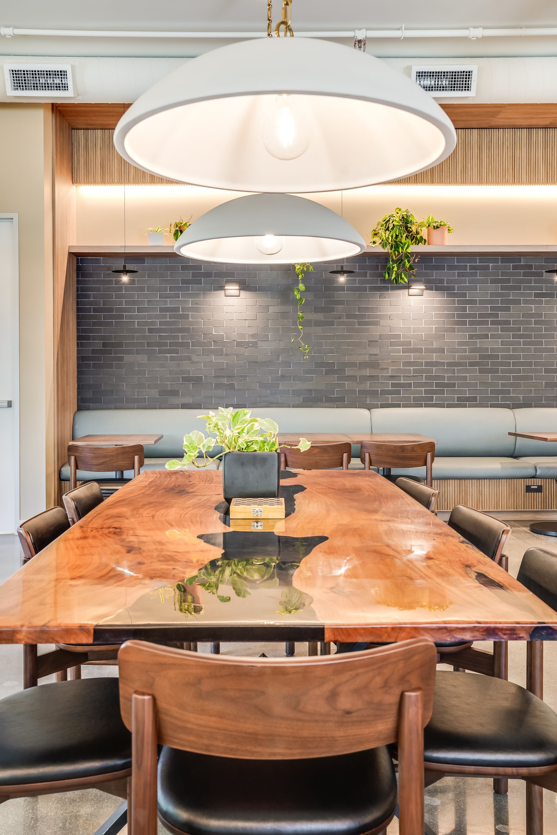 Modern dining room with a long wooden table, pendant lights, benches, and a dark tiled wall